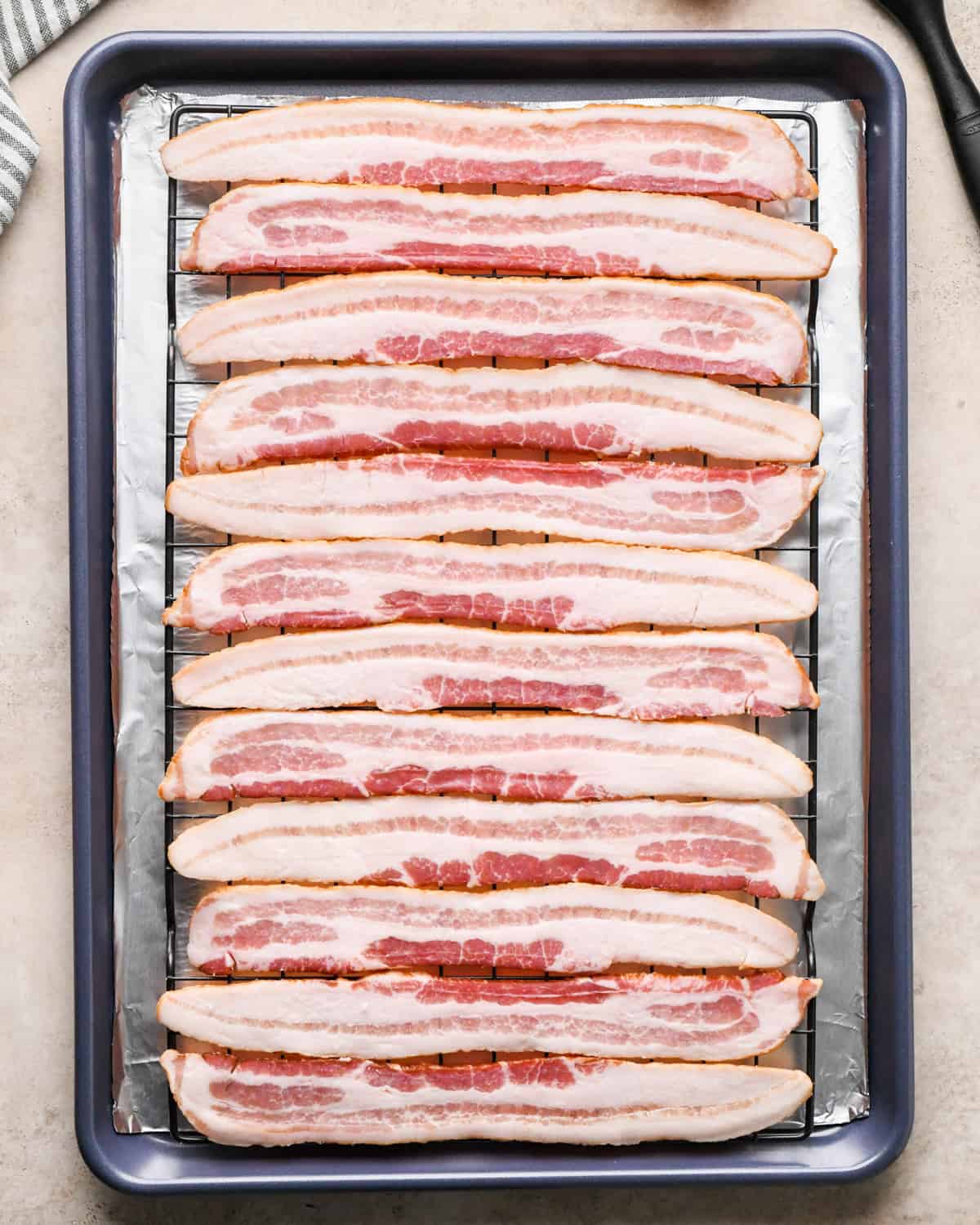 Making maple bacon - overhead photo of a baking sheet topped with tin foil and a cooling rack with bacon strips arranged on top