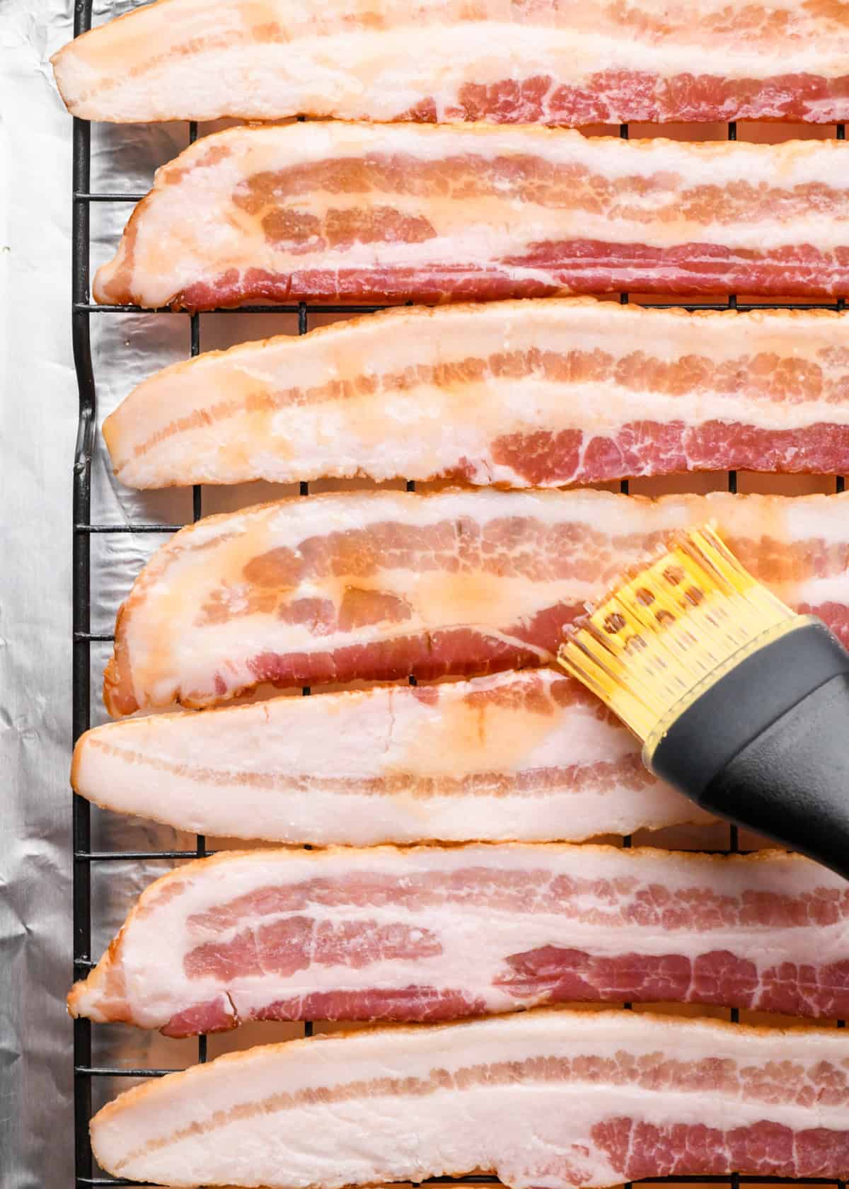 Making maple bacon - overhead photo of maple syrup being spread onto strips of bacon