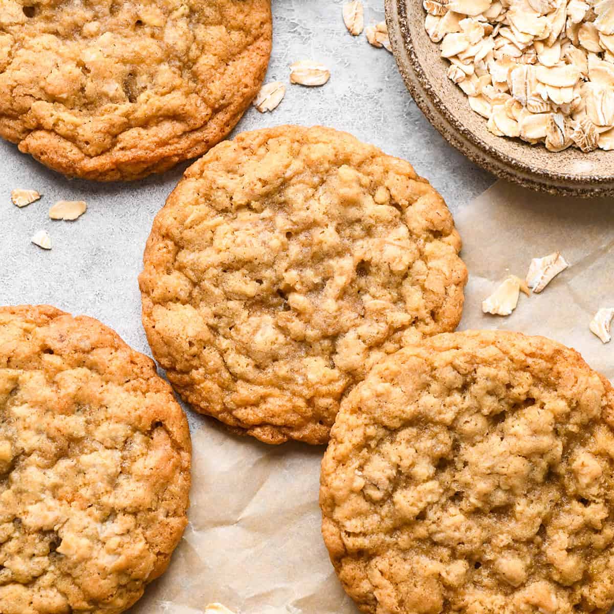 four oatmeal cookies on parchment paper next to a bowl of raw oats