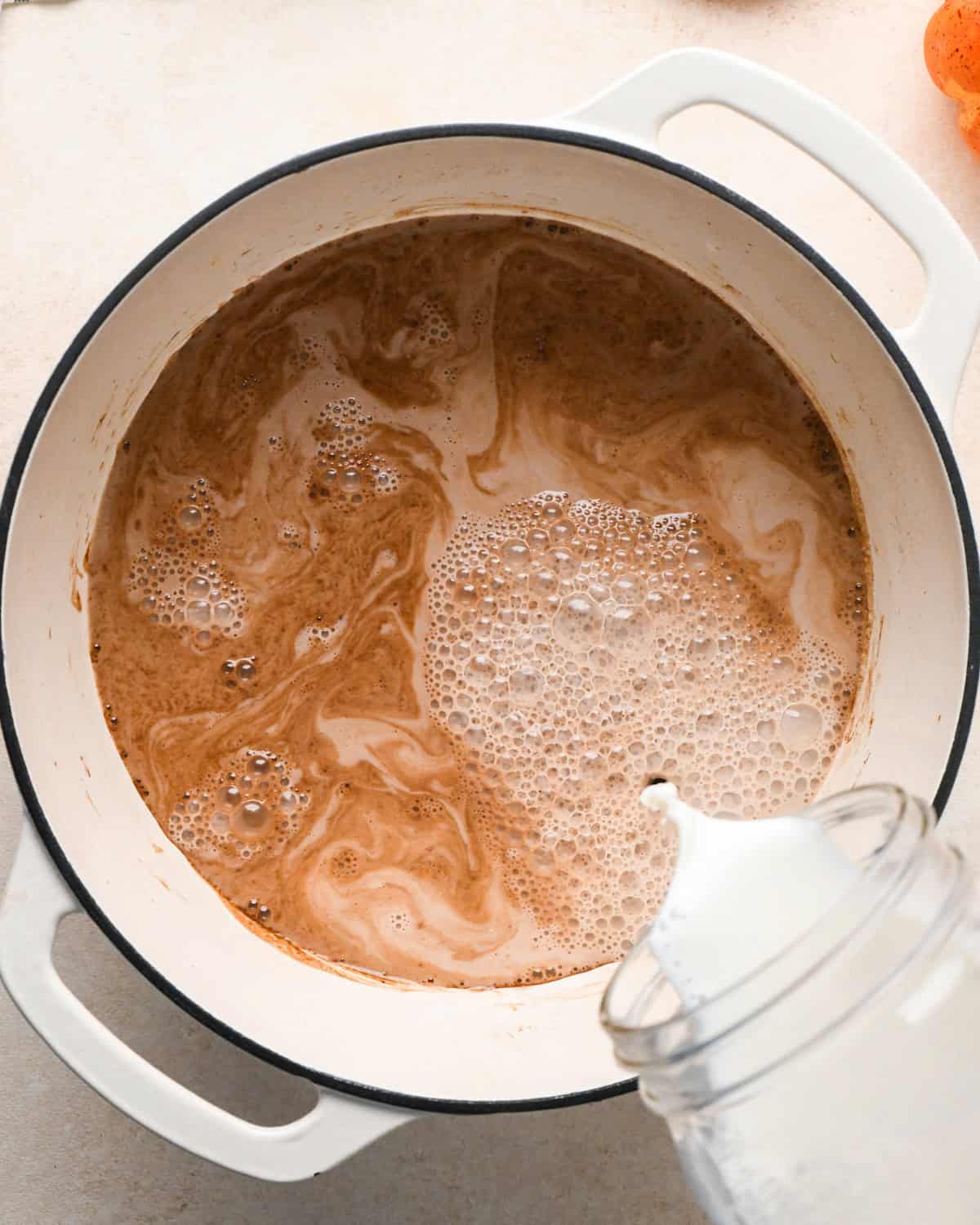 milk being added to the pumpkin spice hot chocolate mixture in a white pot