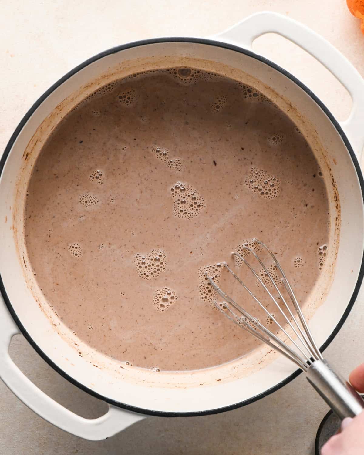 pumpkin spice hot chocolate ingredients being whisked in a white pot
