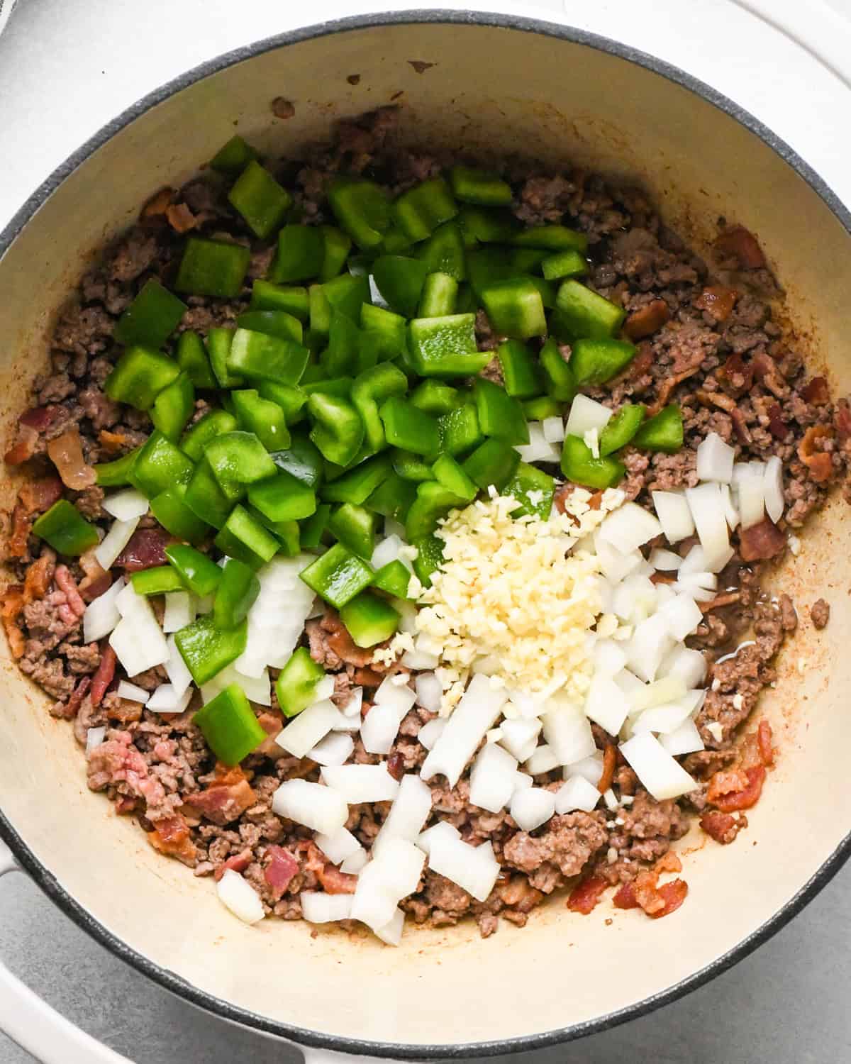 Making bacon chili: onions, bell pepper, and garlic are added to the skillet with bacon and ground beef.
