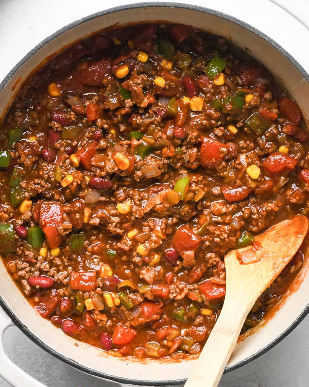 Making bacon chili: meat and vegetables are shown in a pot and cooked, being stirred with a wooden spoon.
