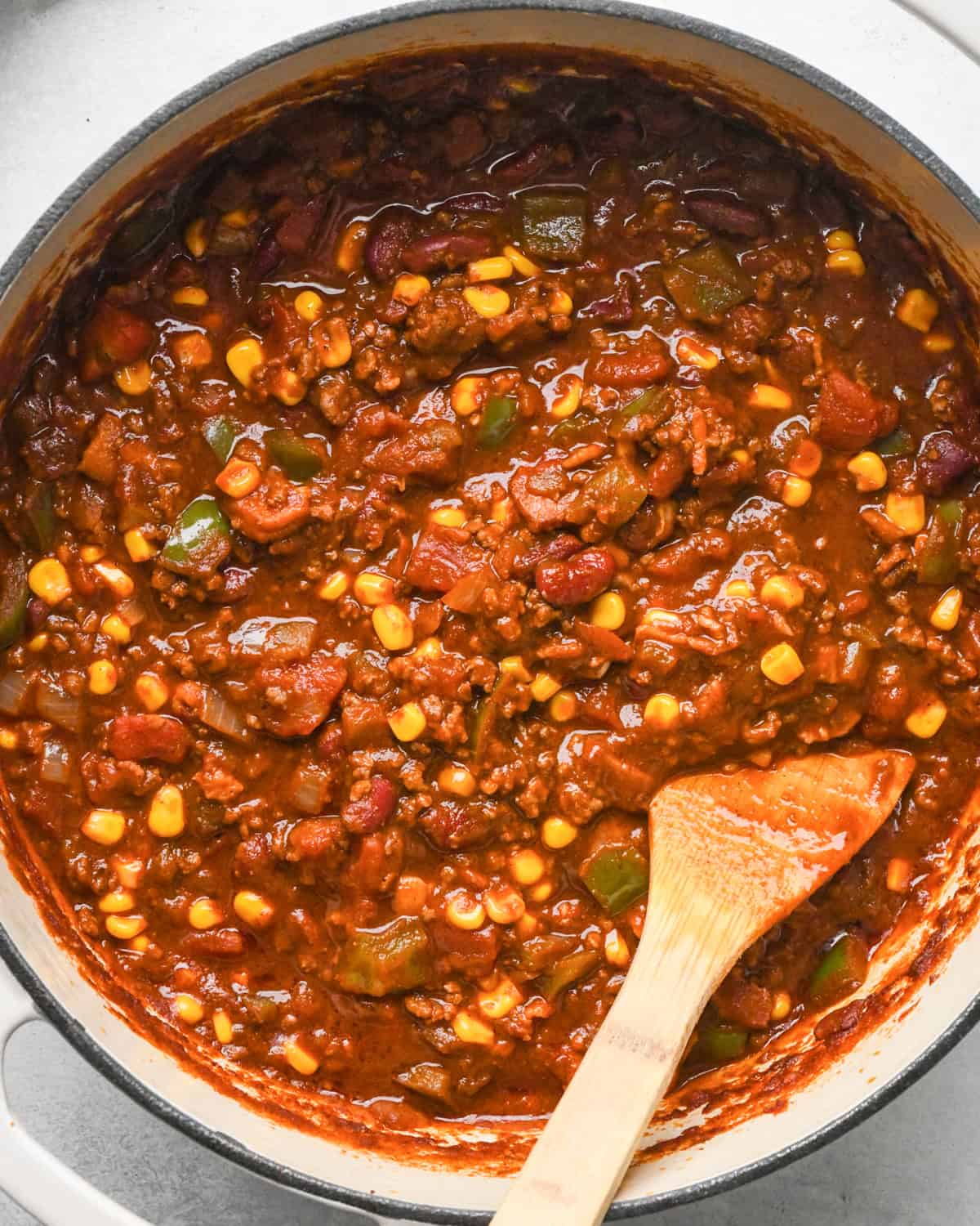 Making bacon chili: up-close photo of completed chili in a pot, being stirred with a wooden spoon and ready to serve.