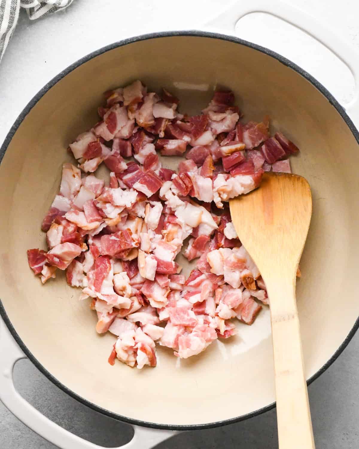 Making bacon chili: cooking bacon in a white skillet, stirring with a wooden spoon.
