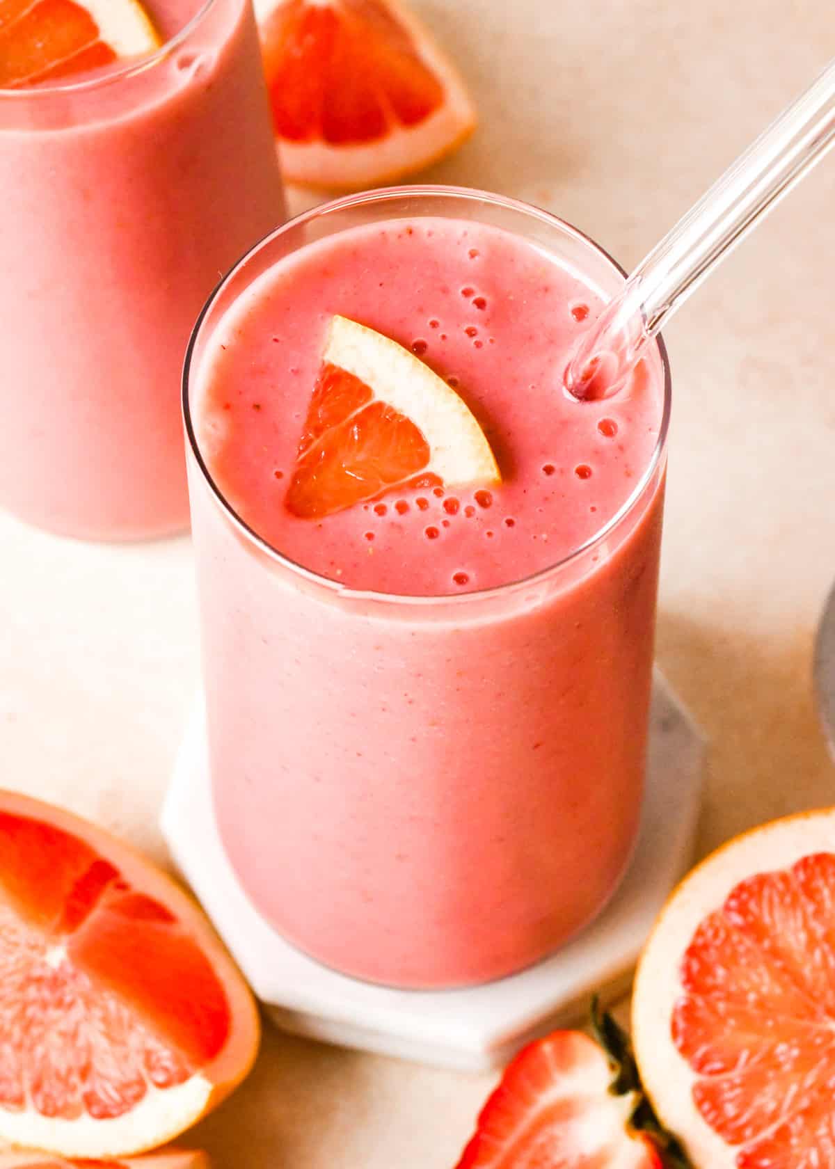 Overview photo of a grapefruit smoothie served in a clear glass with a glass straw, topped with a wedge of fresh grapefruit.