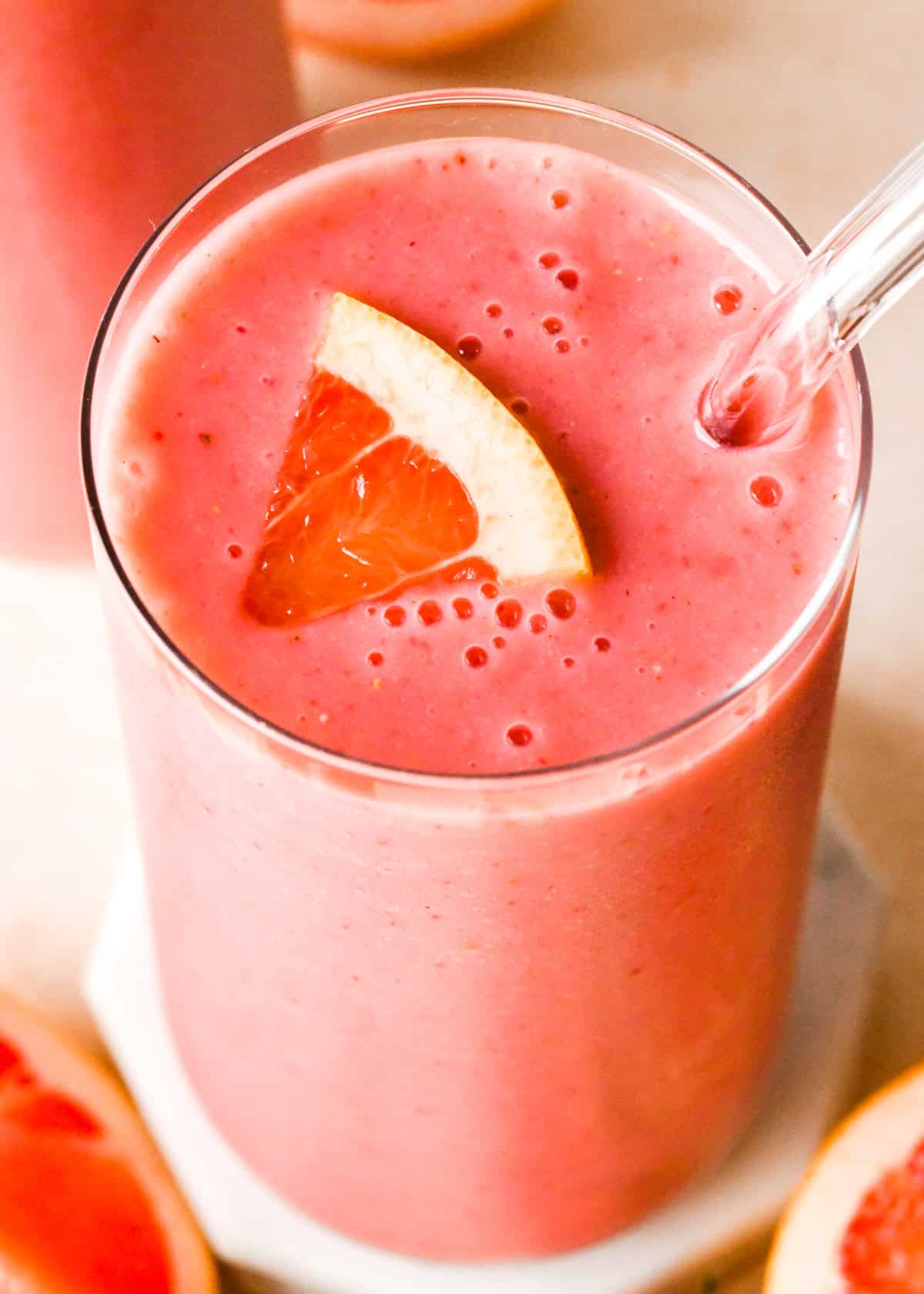 Overview photo of a grapefruit smoothie in a clear glass with a clear straw and topped with a slice of fresh grapefruit.