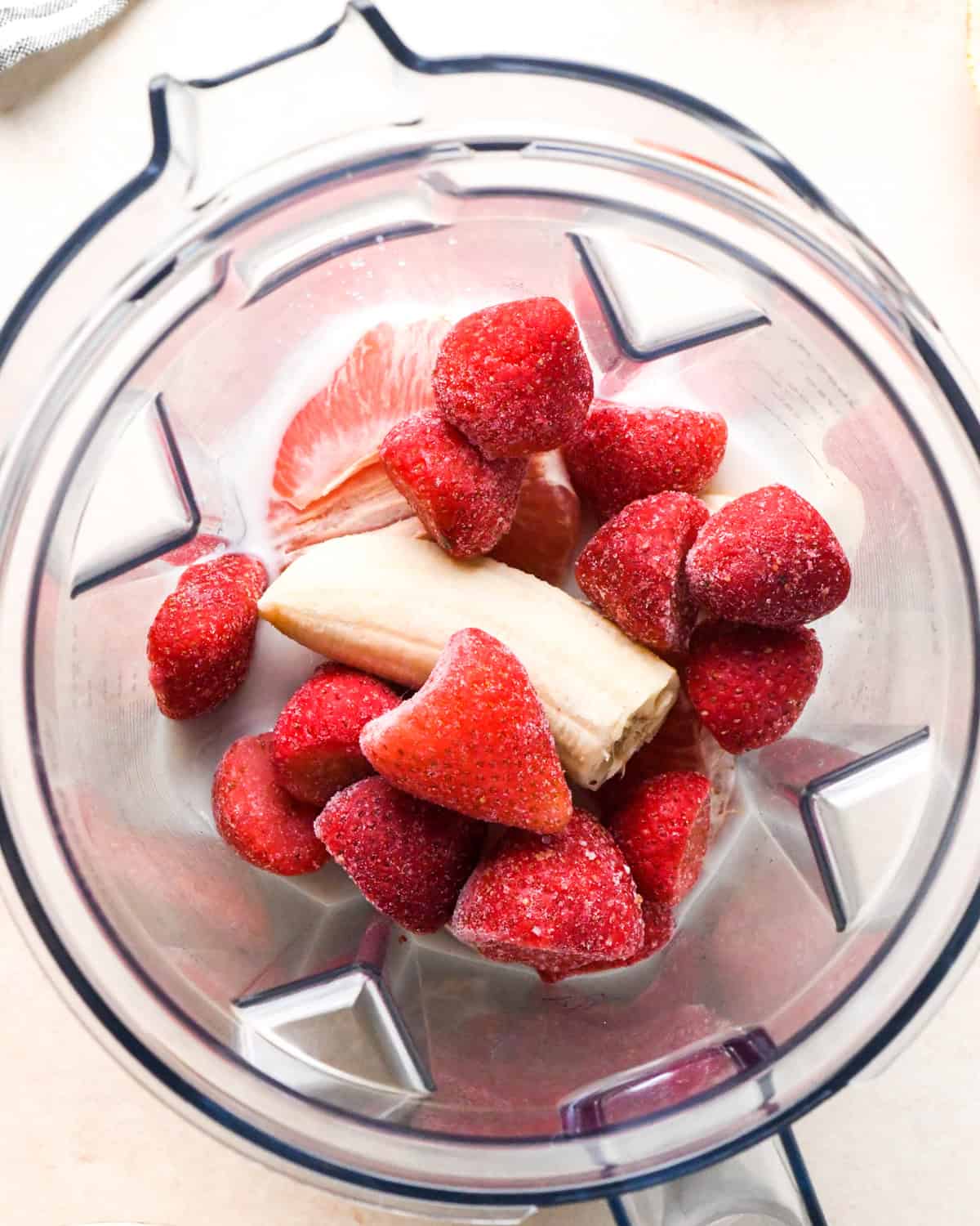 making a grapefruit smoothie: overview photo of milk, grapefruit, frozen banana, and strawberries in a blender.