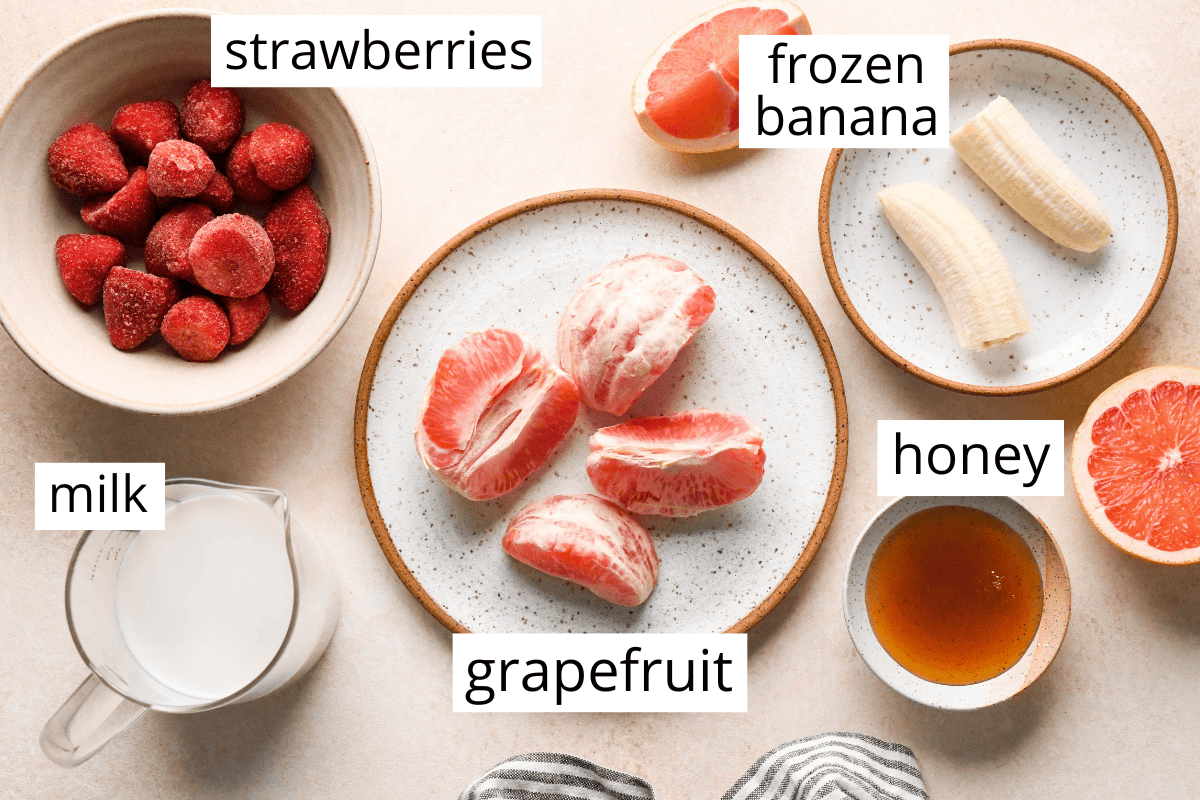 overview photo of the ingredients for this grapefruit smoothie including strawberries, frozen banana, milk, grapefruit, and honey.