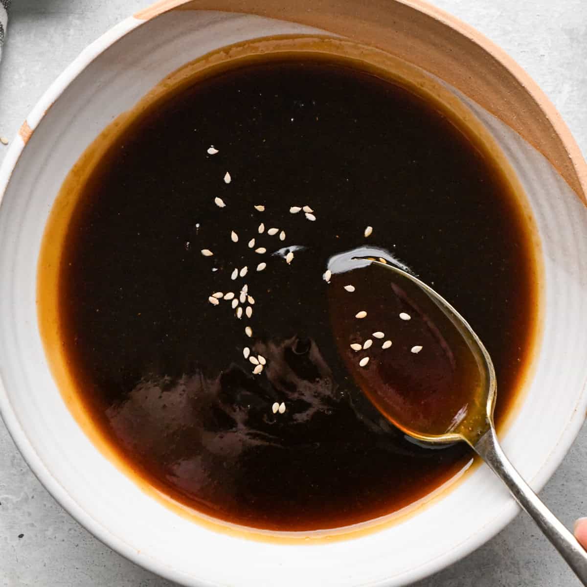 A small bowl of thick homemade teriyaki sauce topped with sesame seeds, with a spoon resting in the sauce.