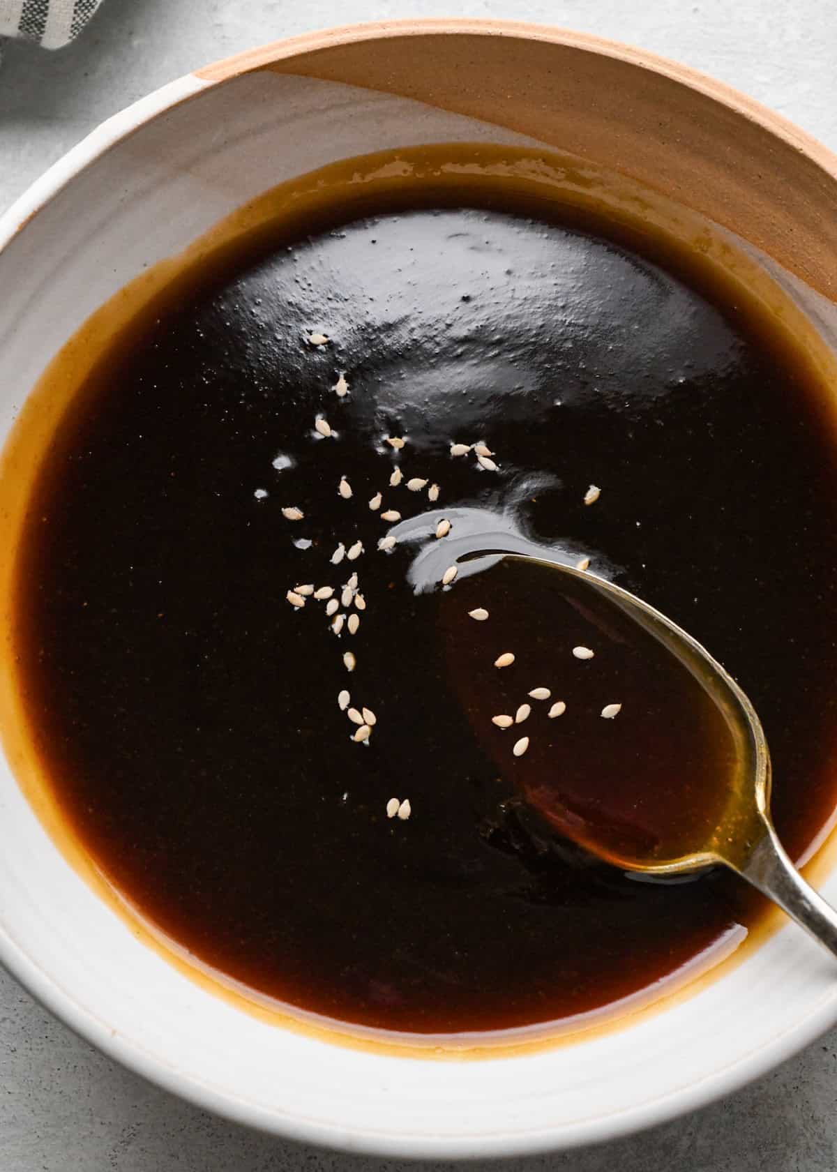 A small bowl of thick homemade teriyaki sauce topped with sesame seeds, with a spoon resting in the sauce.
