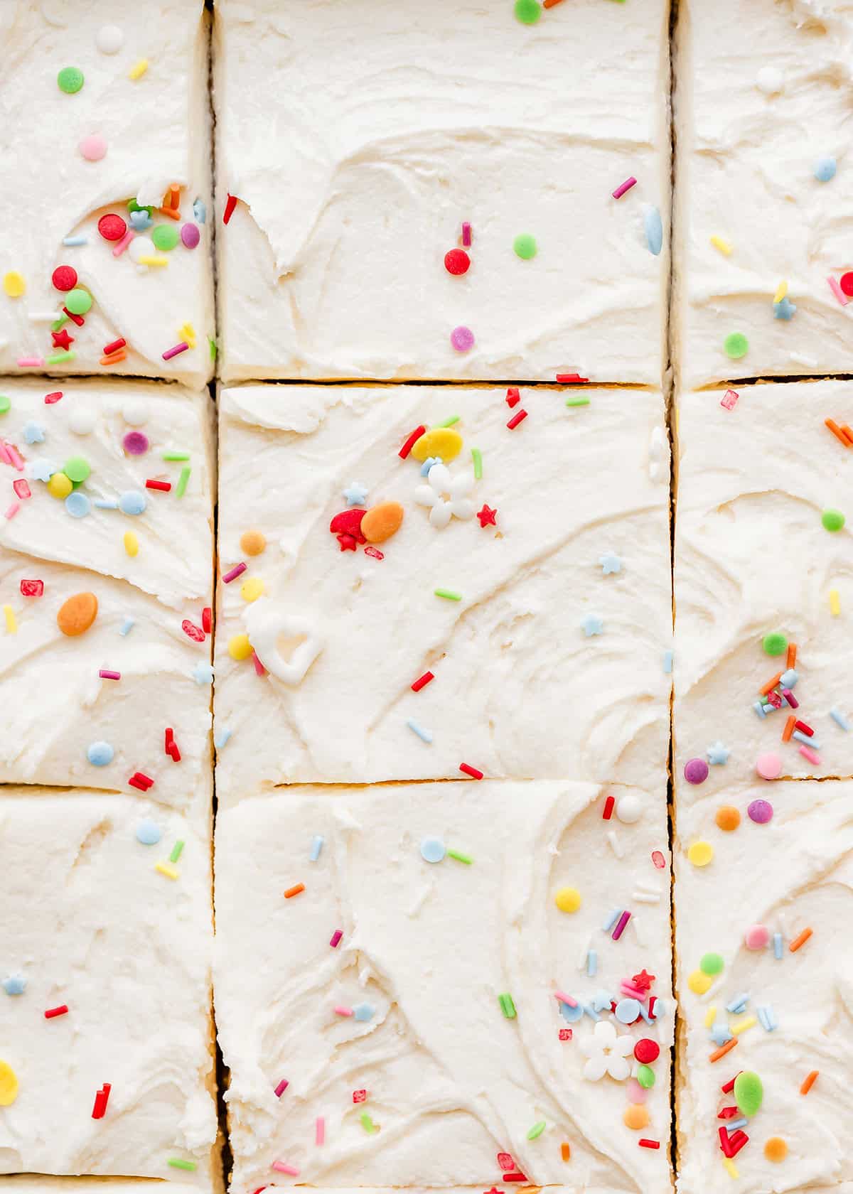 overhead photo of a vanilla sheet cake with frosting and sprinkles cut into pieces 