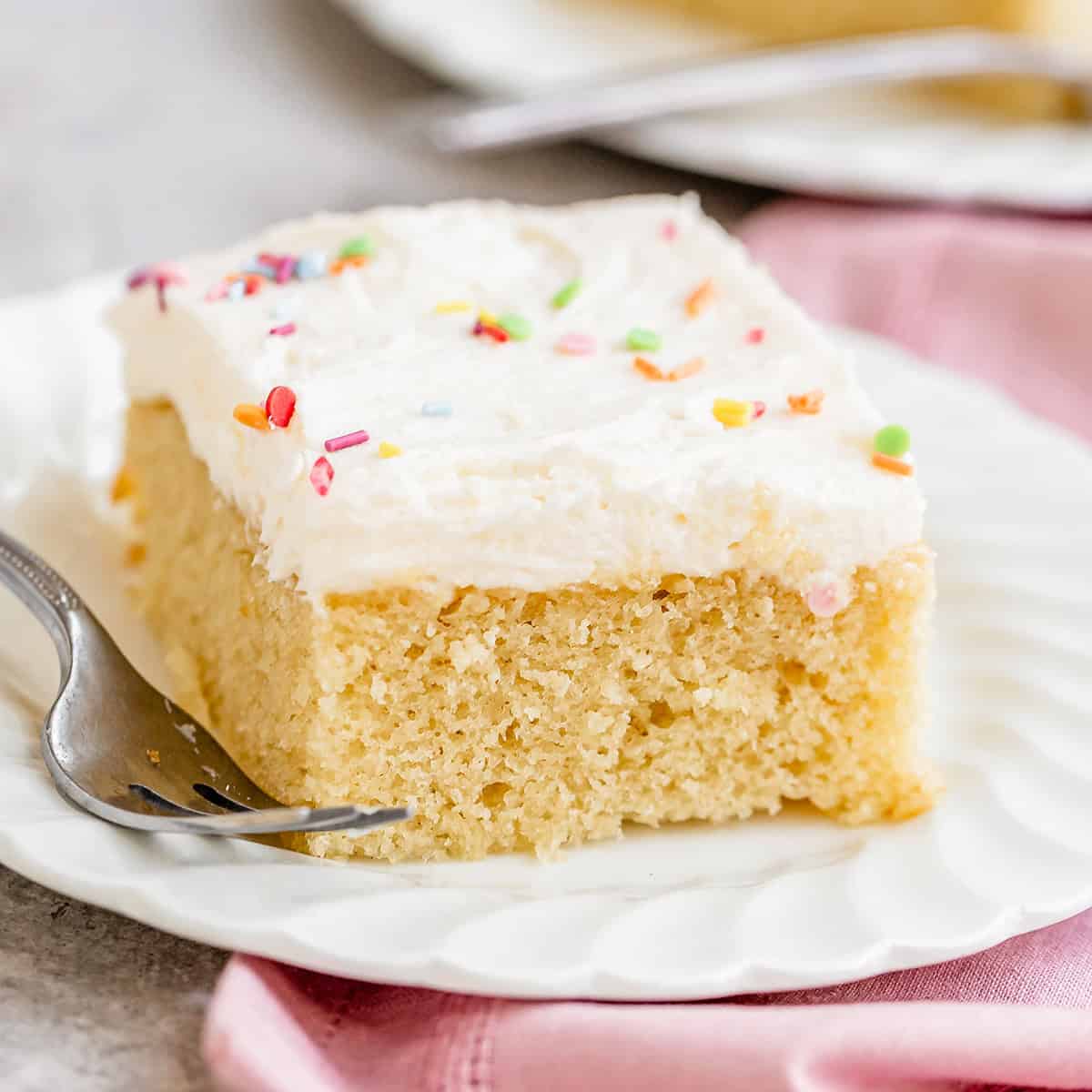 a piece of Vanilla Sheet Cake with white frosting and sprinkles on a plate