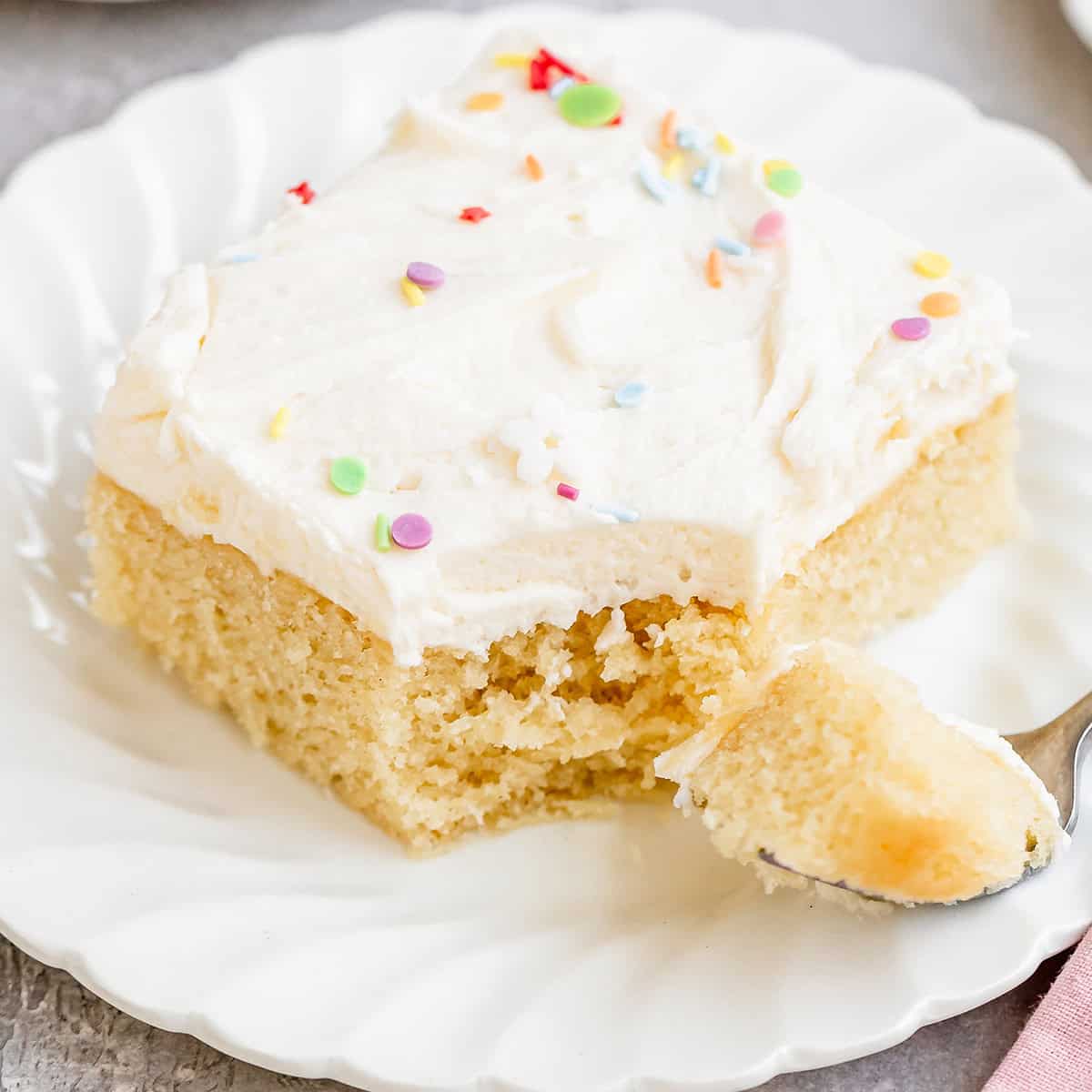 a piece of Vanilla Sheet Cake on a plate with a fork that has a bite on it