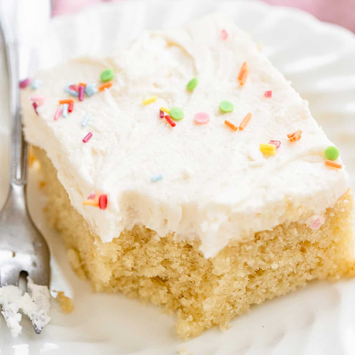 a piece of Vanilla Sheet Cake on a plate with a bite taken out of it 