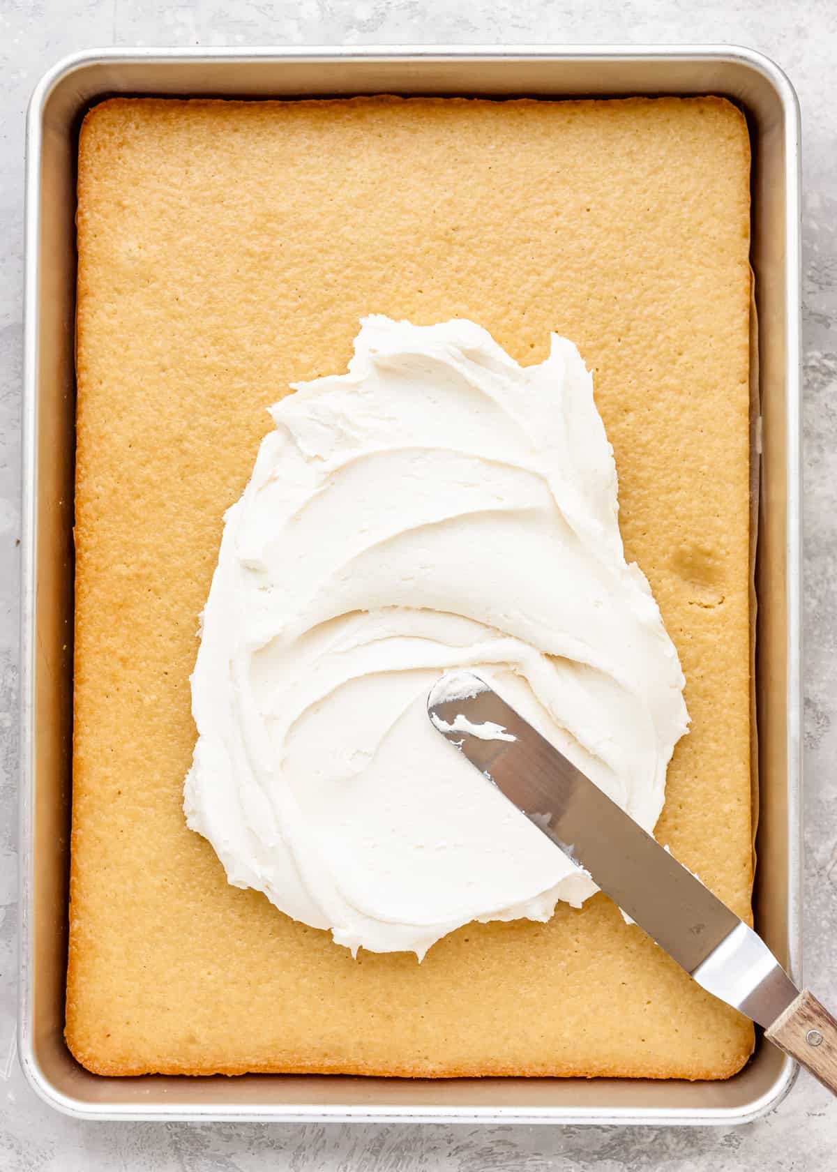 vanilla frosting being spread on top of Vanilla Sheet Cake 