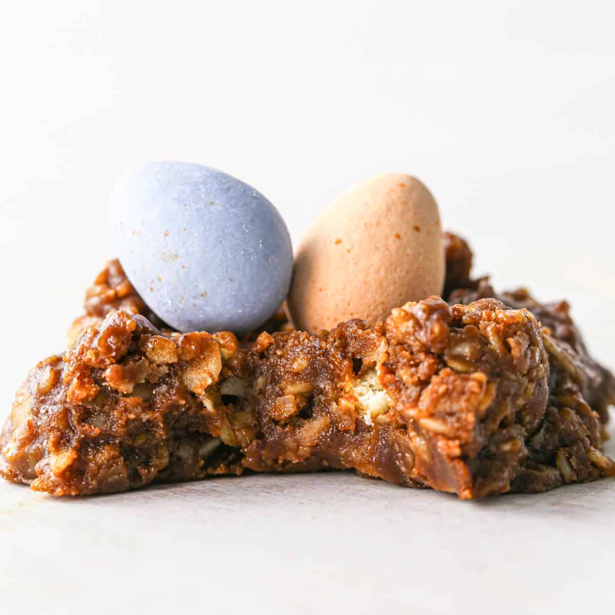 Up-close photo of a bird's nest cookie on a white surface with a bite taken out.