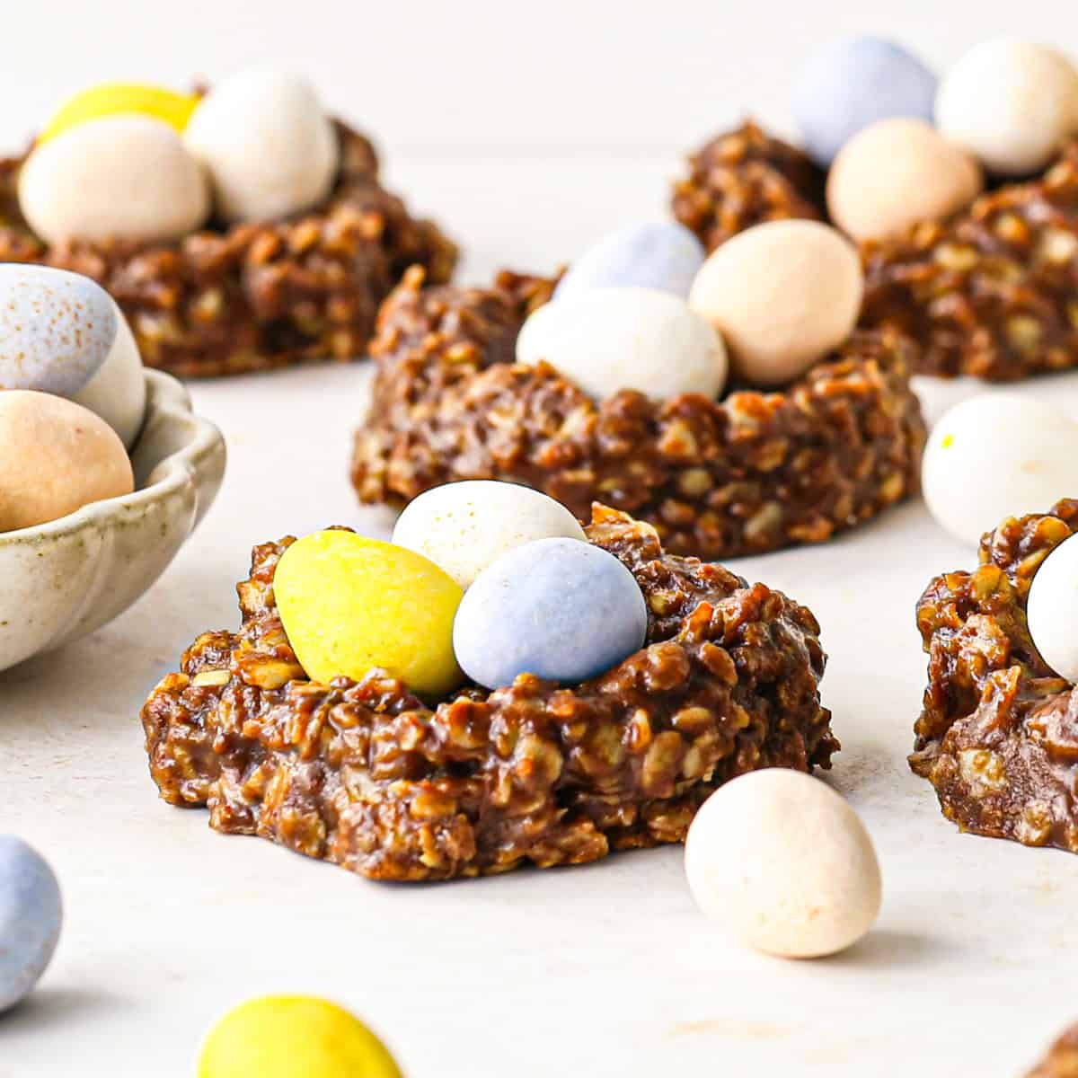 Up-close photo of a bird's nest cookie on a white surface. It is surrounded by additional cookies and candy eggs.
