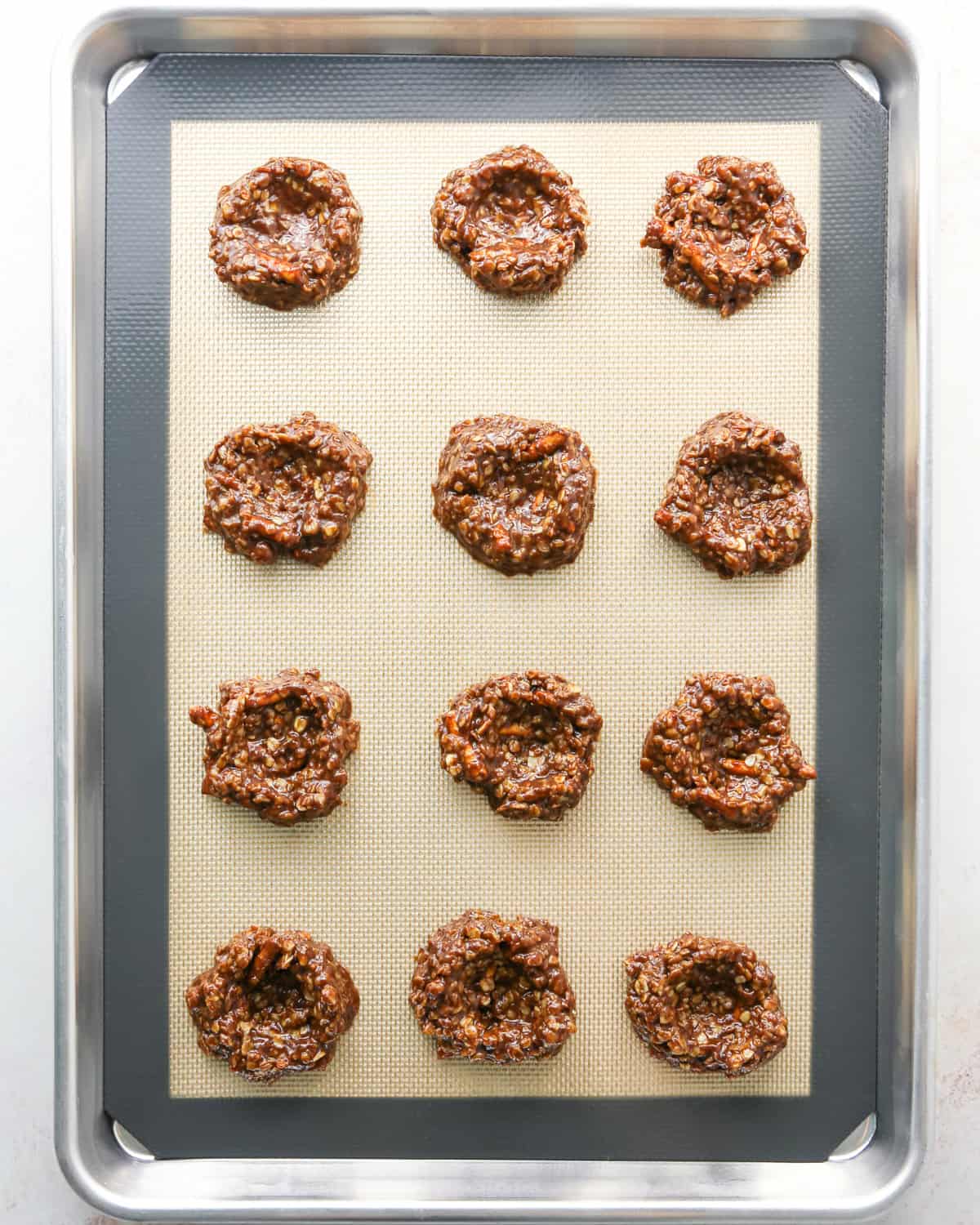 Making bird's nest cookies: overhead photo of 12 balls of cookie dough on a metal baking sheet. Each cookie dough ball has an indent made by a cookie scoop.