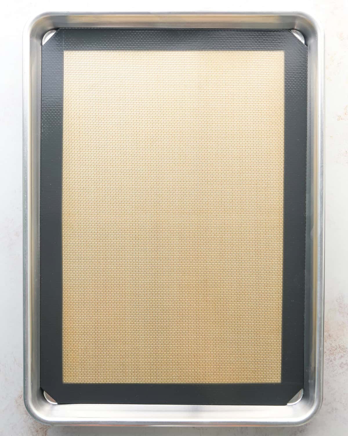 Making bird's nest cookies: overhead photo of a metal baking sheet on a white countertop with a silicone baking sheet on top.