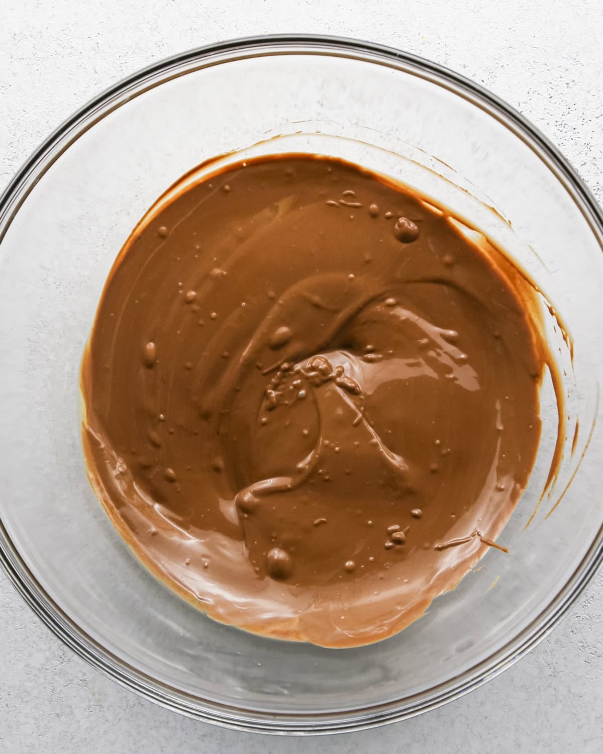 Making Haystack Cookies: overhead photo of semisweet chocolate chips, butterscotch chips, and peanut butter added to a large clear bowl and melted together.