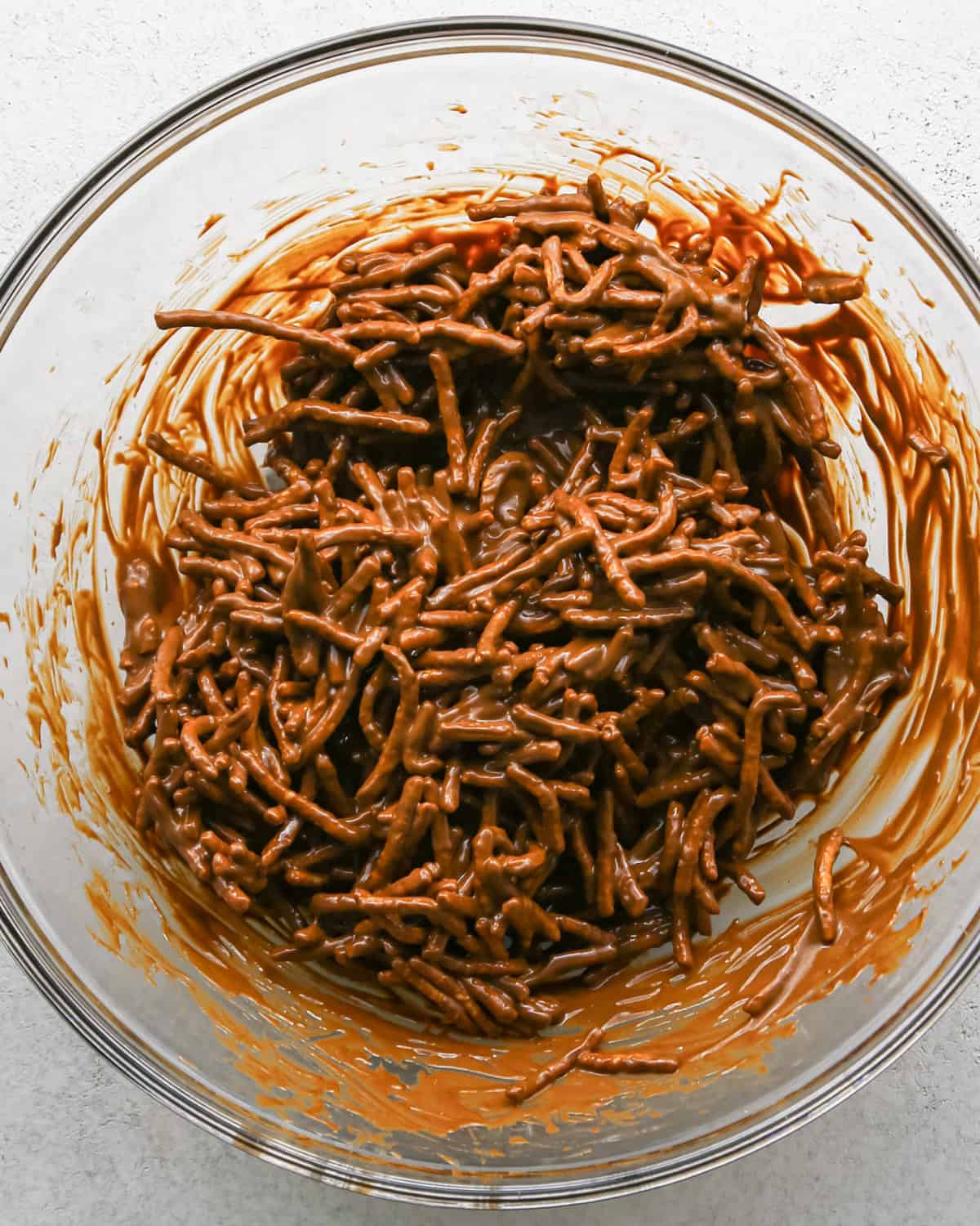 Making Haystack Cookies: overhead photo of chow mein noodles added to melted mixture of peanut butter, semisweet chocolate chips, and butterscotch chips in a large clear bowl and mixed together.