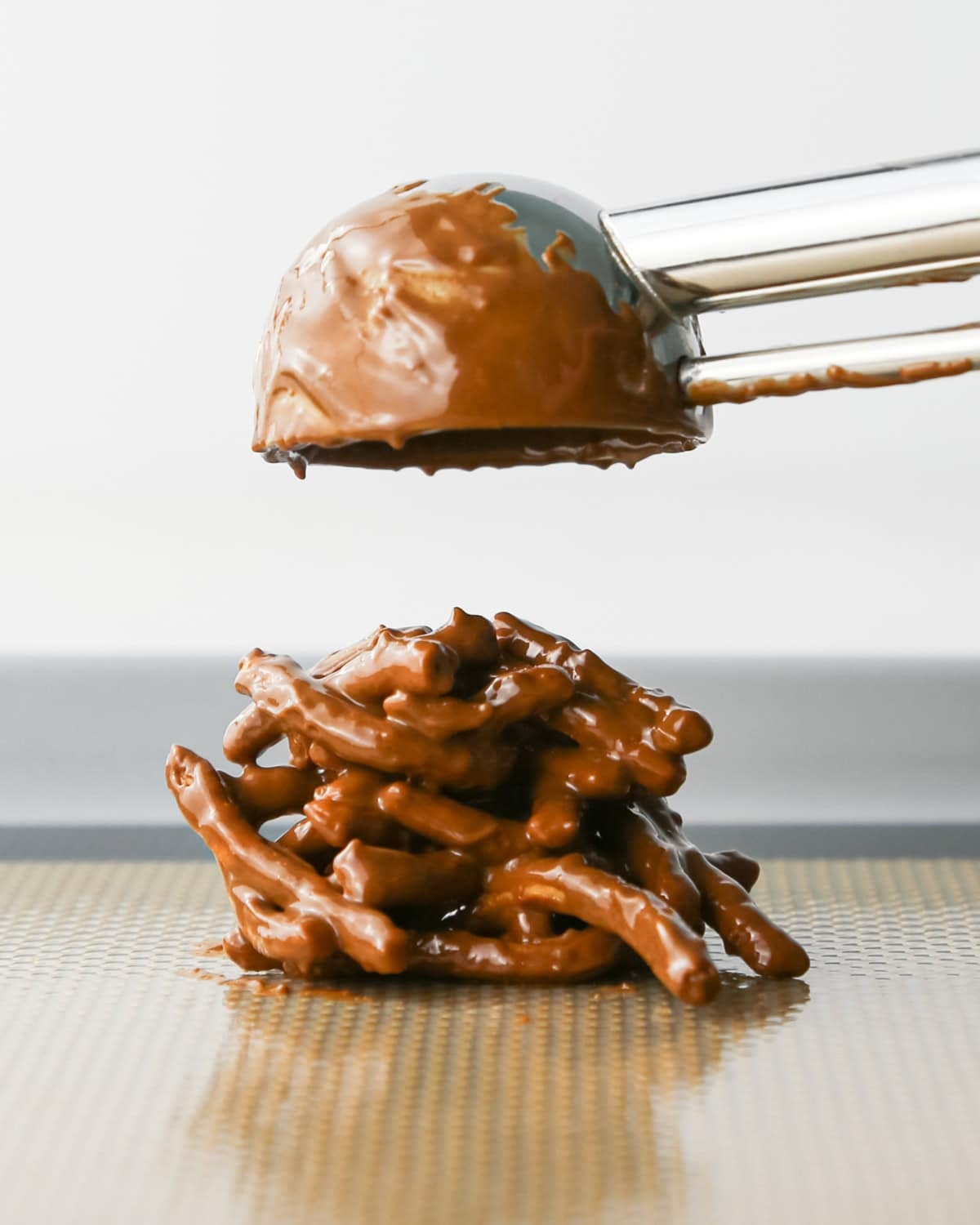Making Haystack Cookies: overhead photo of a cookie scoop dropping a scoop of semisweet Haystack Cookie mixture onto a baking sheet.