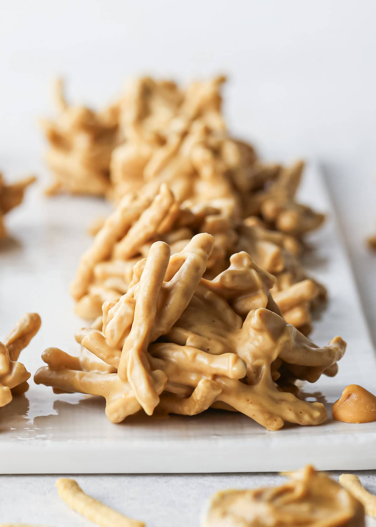 Close-up of peanut butter haystack cookies made with crunchy chow mein noodles and sitting on a white surface.