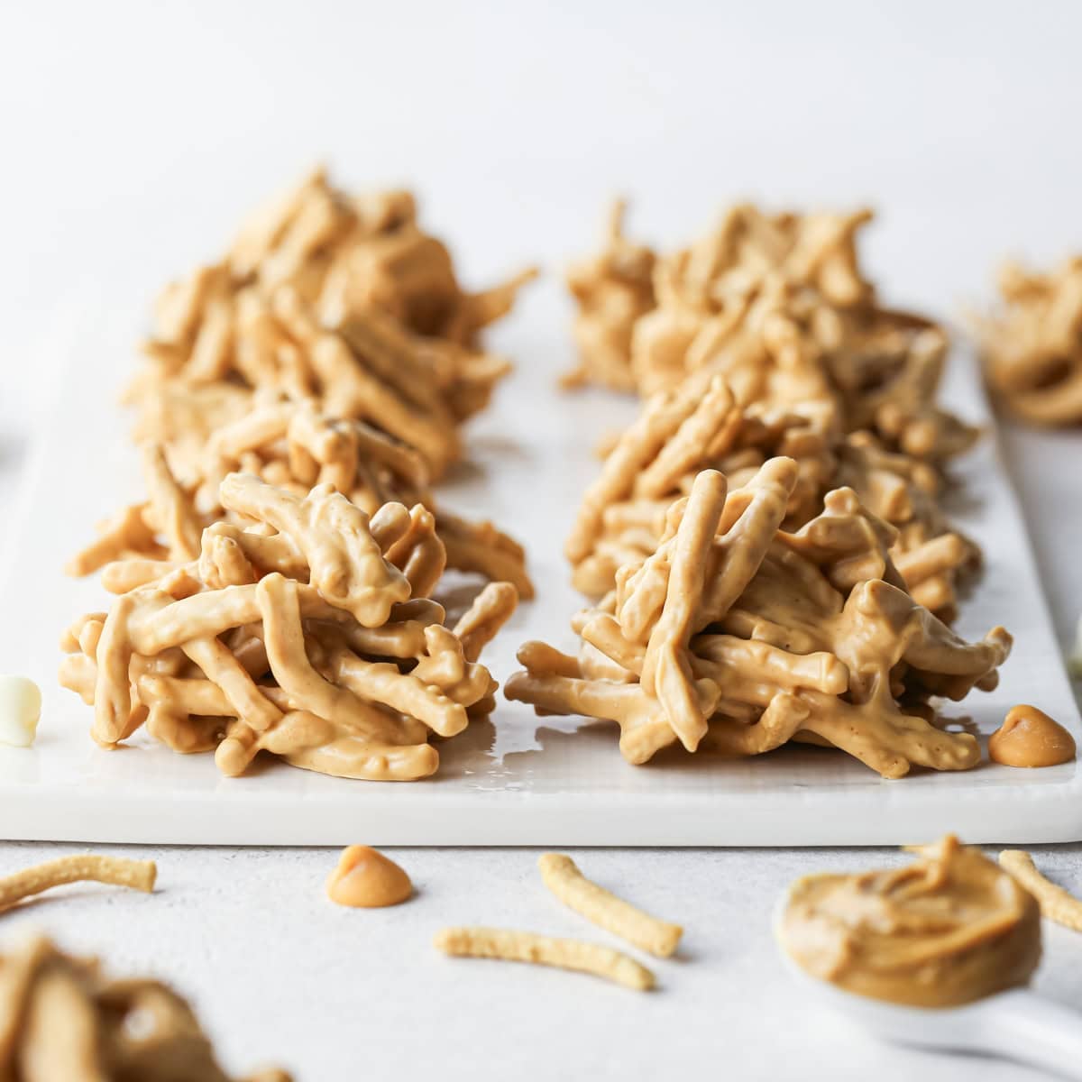 Close-up of white chocolate haystack cookies made with crunchy chow mein noodles sitting on a white surface.
