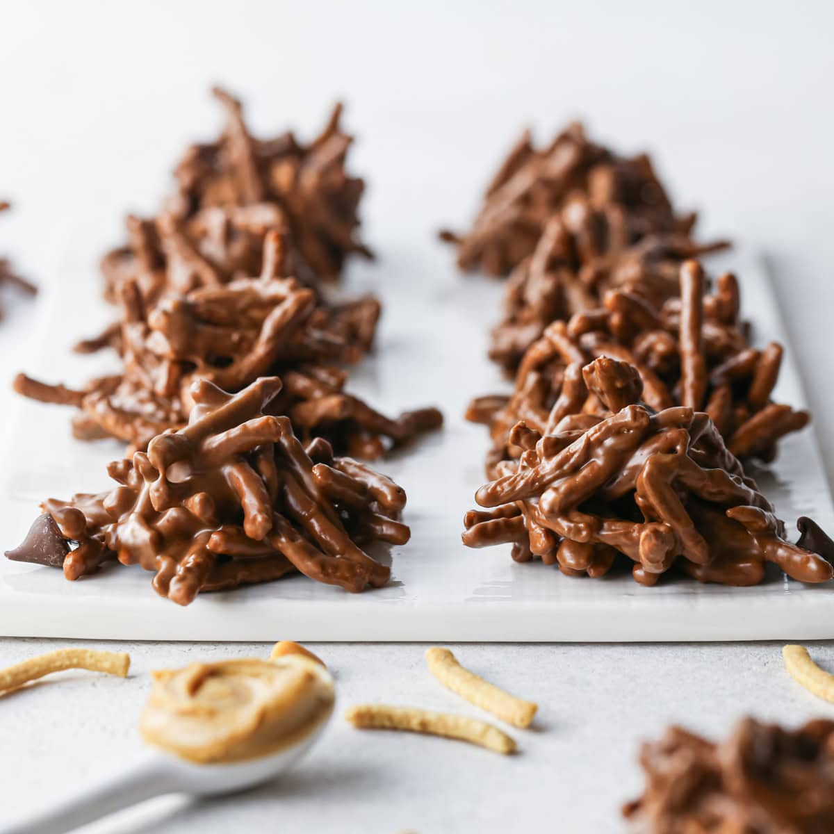 Close-up of chocolate haystack cookies made with crunchy chow mein noodles sitting on a white surface.
