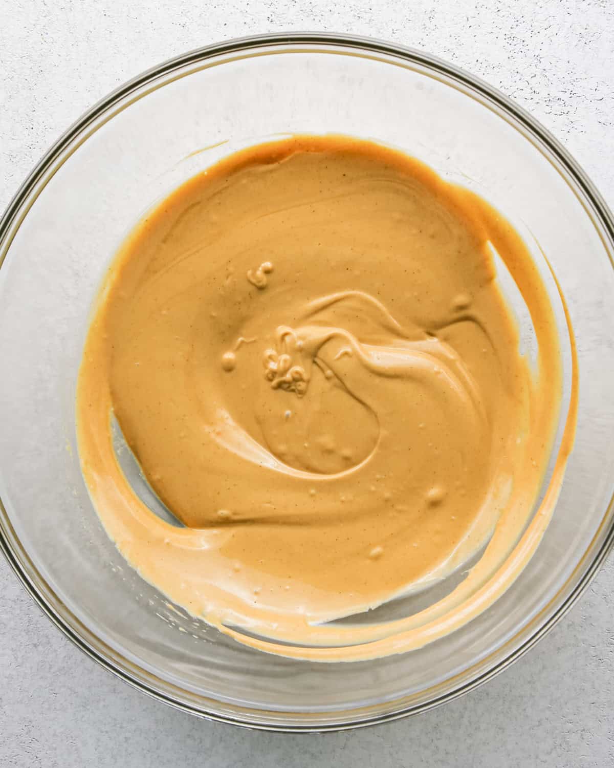 Making Haystack Cookies: overhead photo of white chocolate chips, butterscotch chips, and peanut butter added to a large clear bowl and melted together.