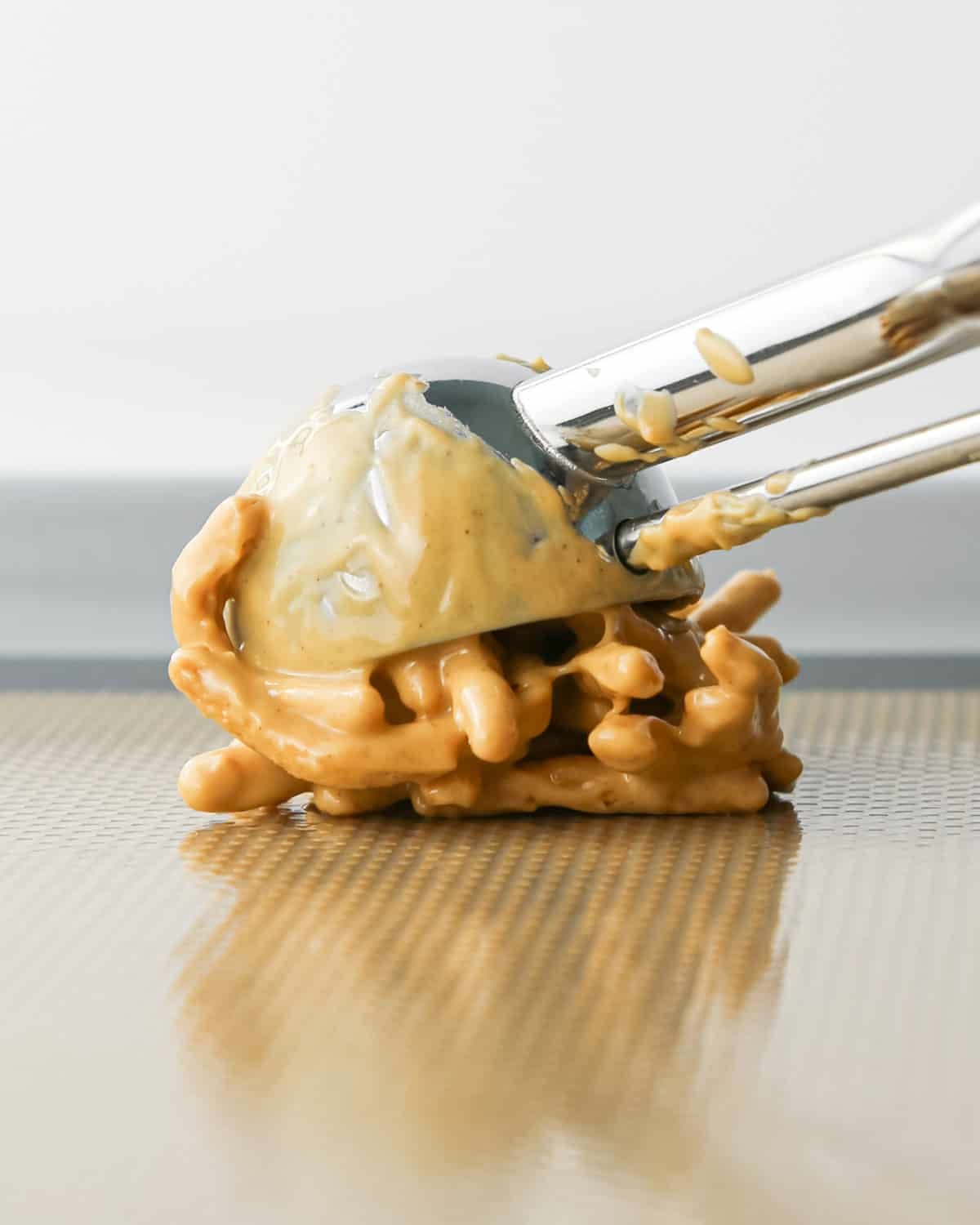 Making Haystack Cookies: overhead photo of a cookie scoop dropping a scoop of white chocolate Haystack Cookie mixture onto a baking sheet.