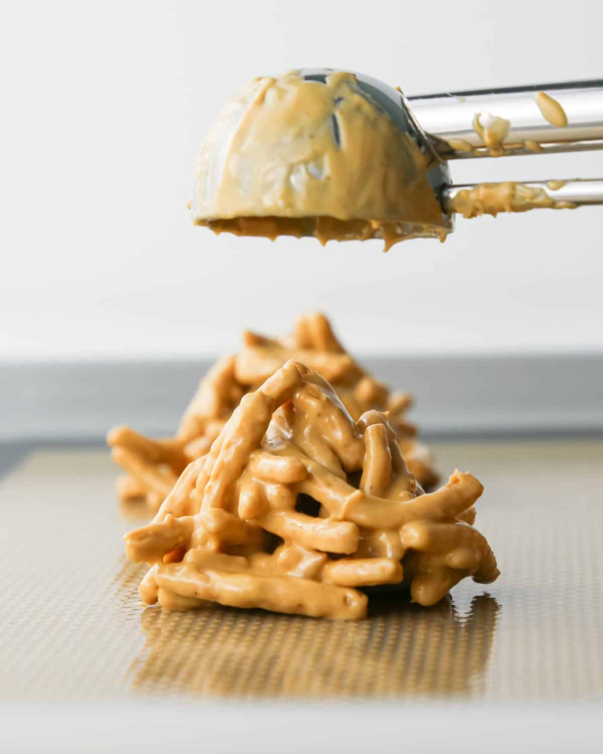 Making Haystack Cookies: overhead photo of a cookie scoop dropping a scoop of white chocolate Haystack Cookie mixture onto a baking sheet.