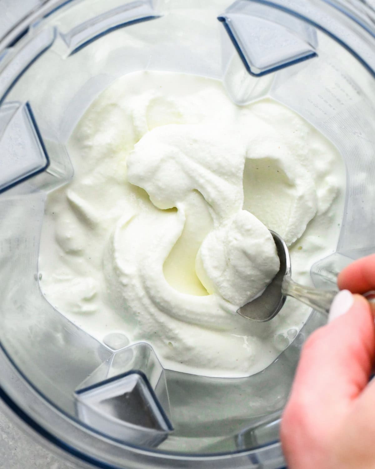 a hand using a spoon to scoop shamrock shake in a blending container after blending