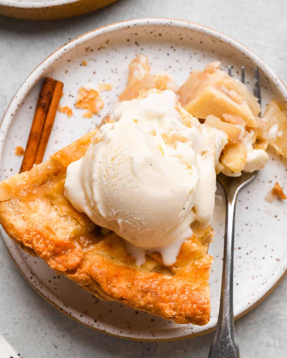 a piece of pear pie with vanilla ice cream and a fork taking a bite out of it on a plate with a cinnamon stick