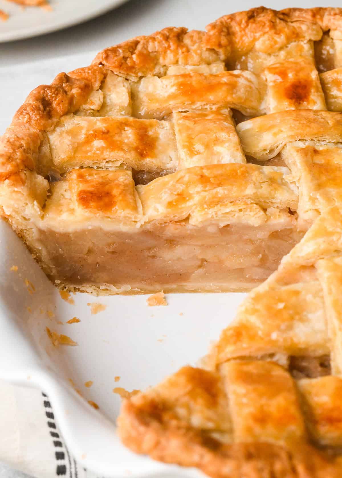 close up of pear pie with a lattice crust in a white pie dish with one slice cut out of it so the pear pie filling is visible