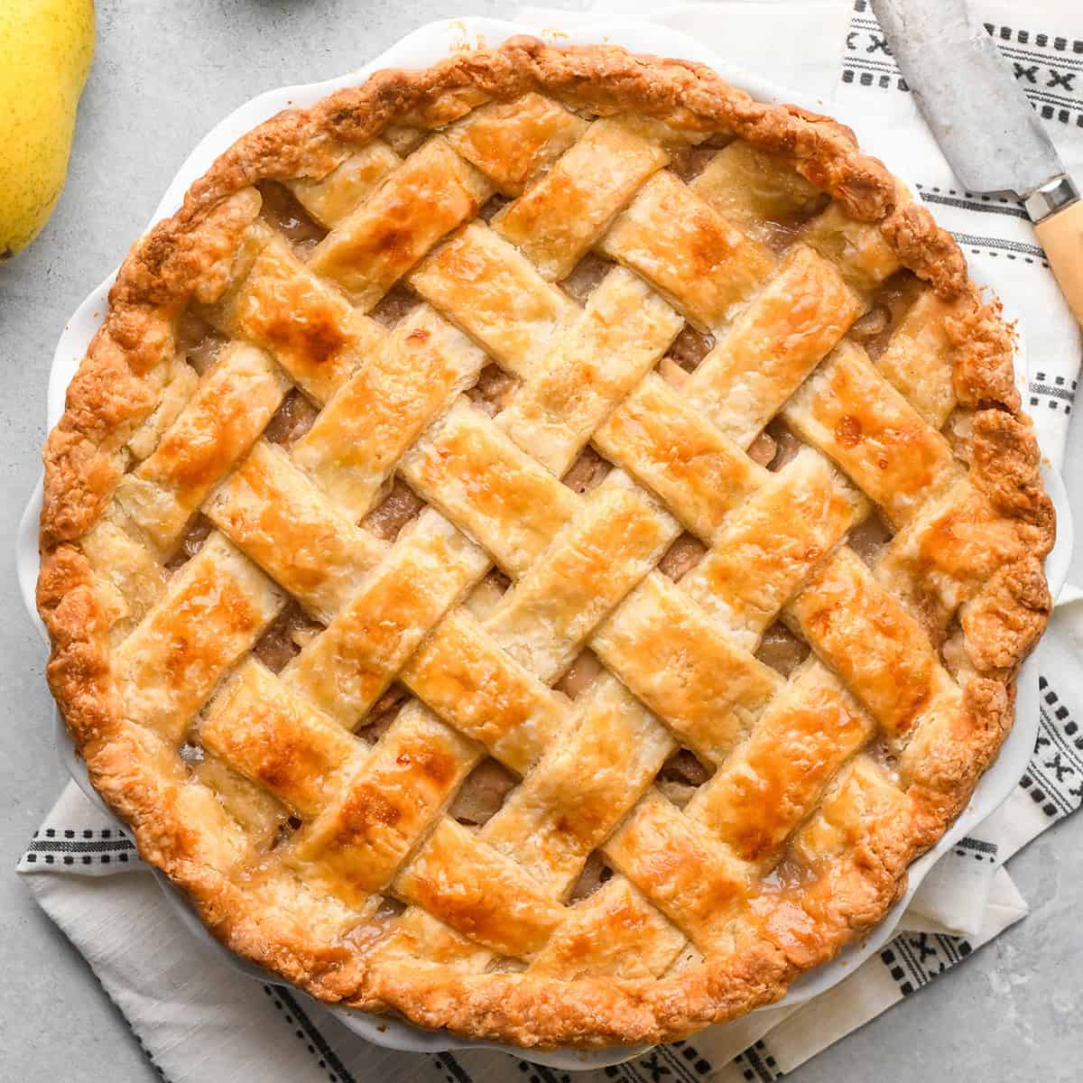 lattice pie crust in a pie dish after baking on a gray surface with a black and white towel