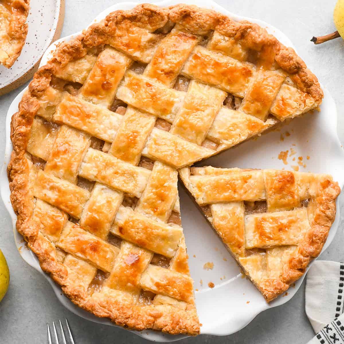 a pie in a pie dish with a Lattice Pie Crust - with a slice cut out still in the dish on a gray surface