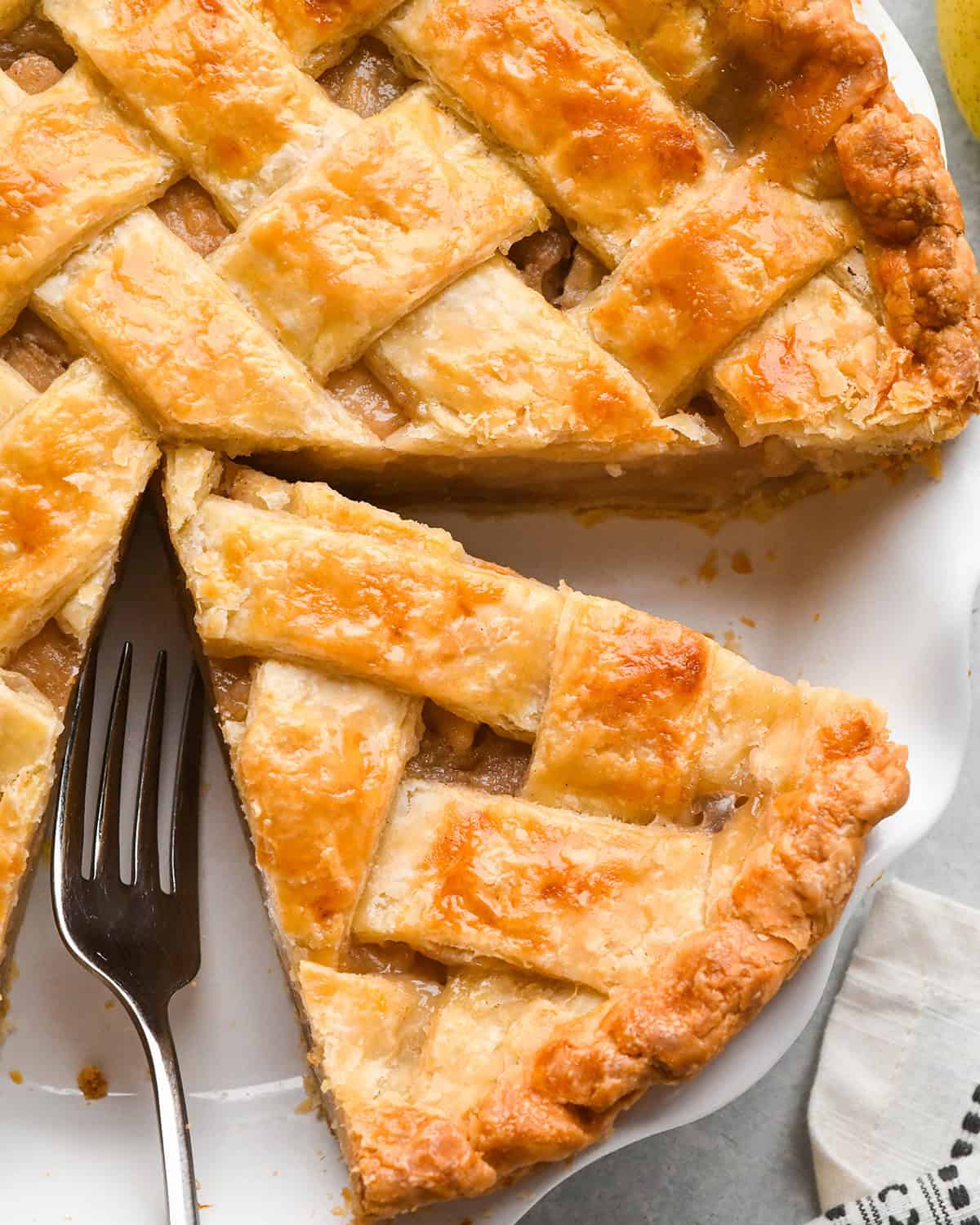 up close photo of a piece of pie with a lattice pie crust in a white pie dish with the rest of the pie and a fork