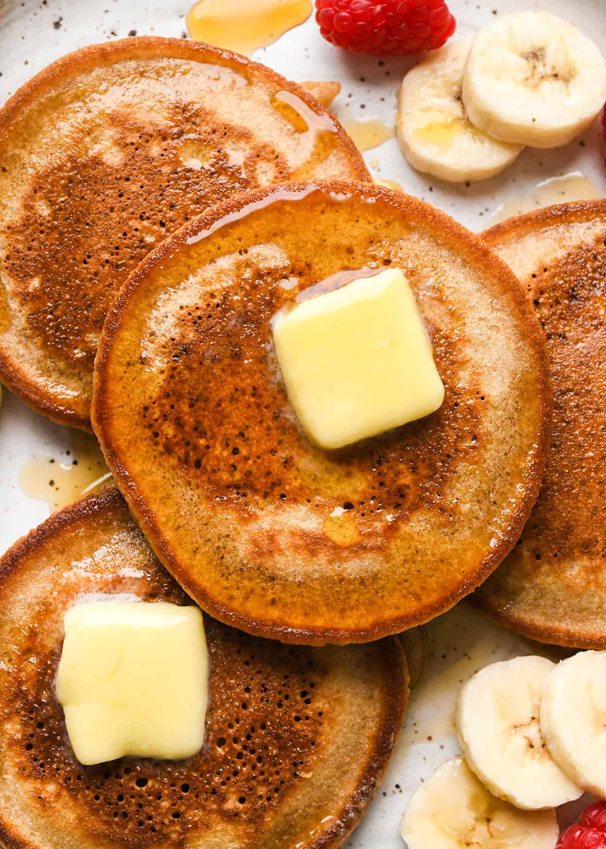 4 Oat Flour Pancakes on a plate with butter, syrup, bananas and raspberries