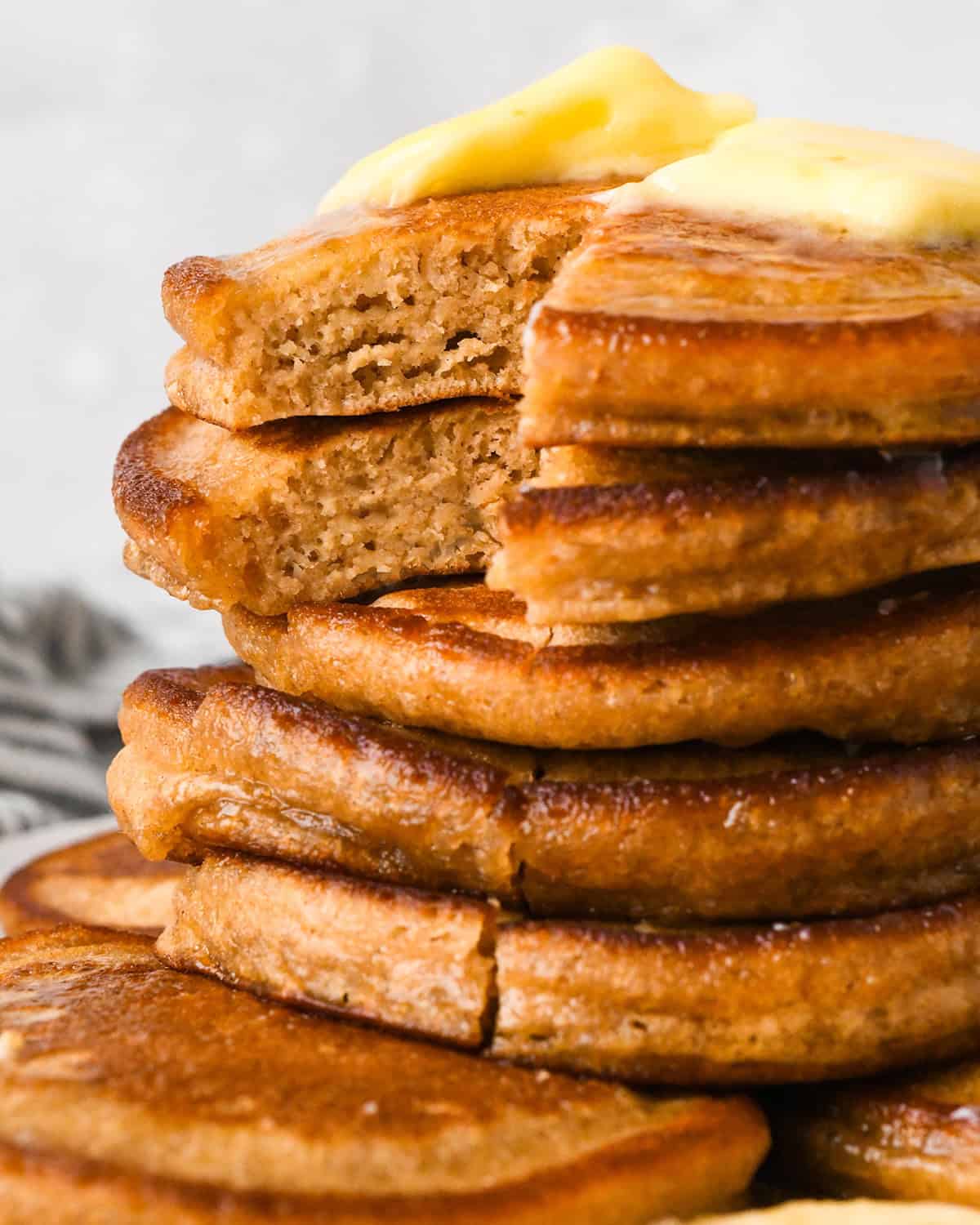 a stack of 5 Oat Flour Pancakes, the top two with bites cut out of them so the fluffy texture is visible topped with melted butter and syrup