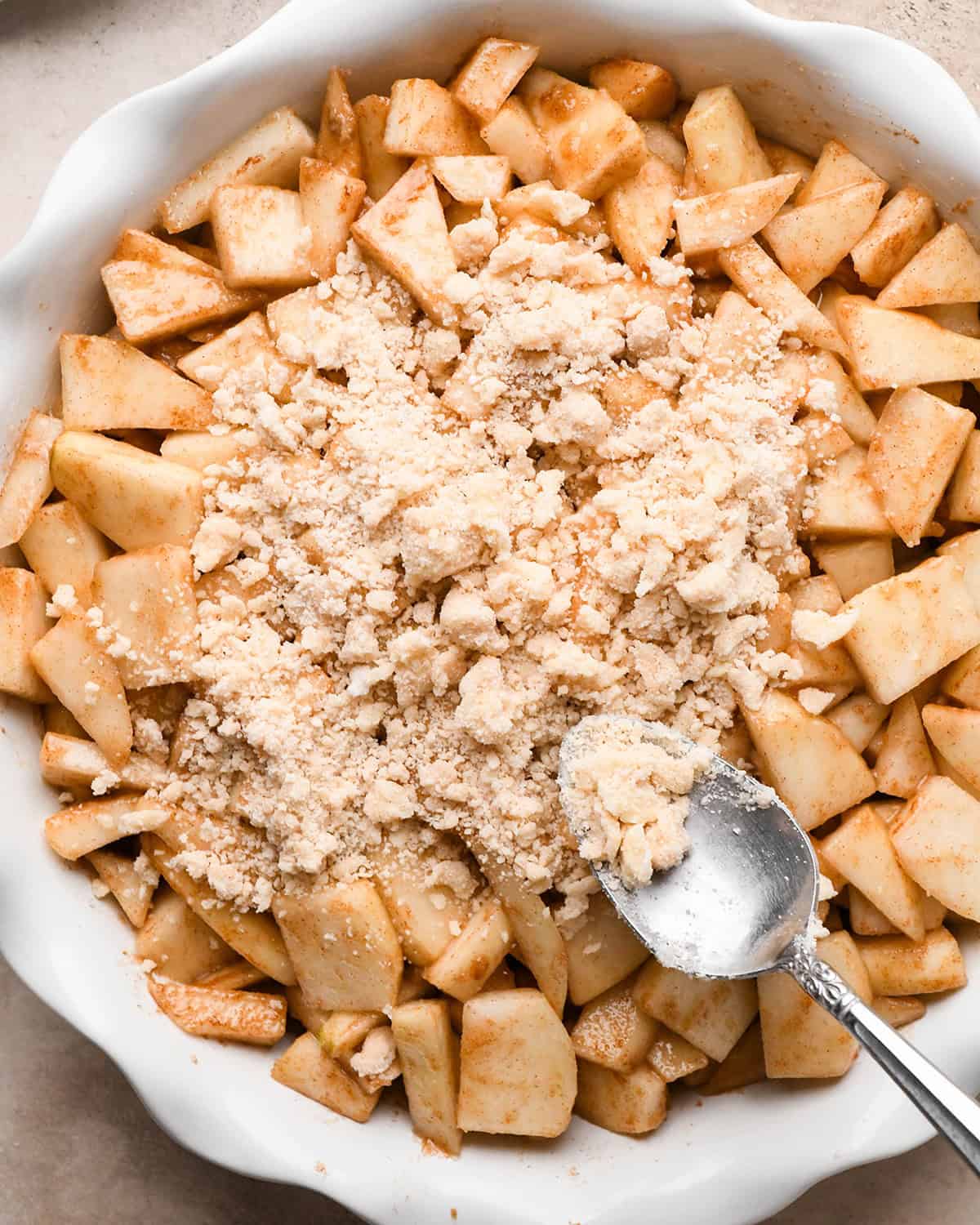 sprinkling pear crumble topping over filling in a pie dish