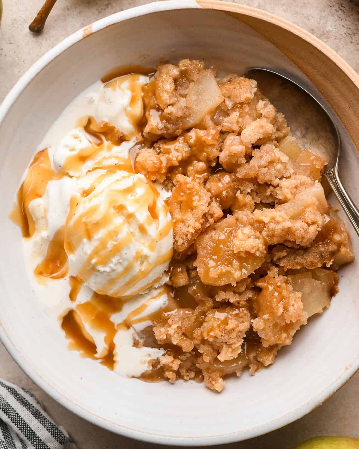 Pear Crumble in a bowl with vanilla ice cream, caramel sauce and a spoon