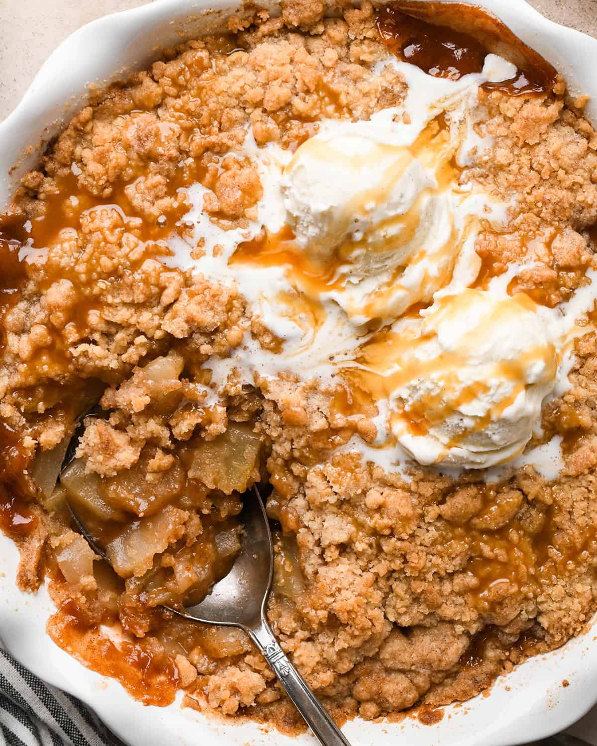 Pear Crumble in a pie dish with a serving spoon, two scoops of vanilla ice cream and caramel sauce 