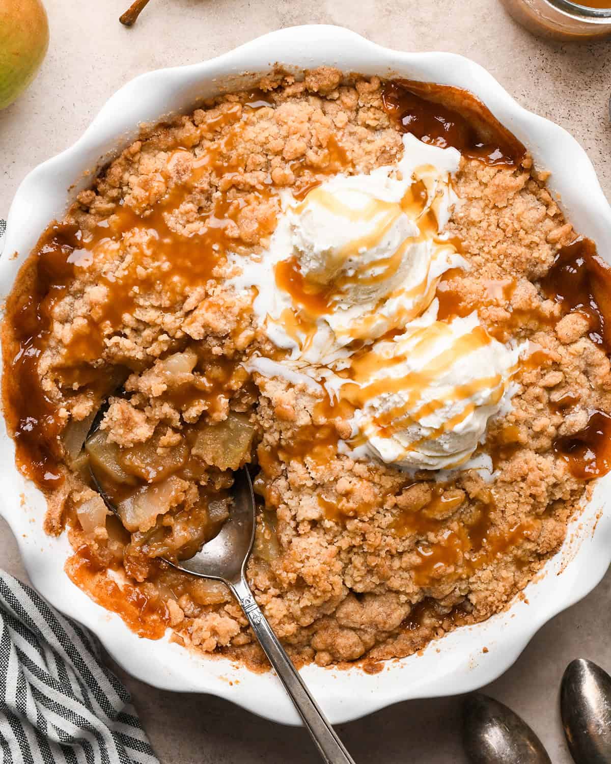 Pear Crumble in a pie dish with a serving spoon, two scoops of vanilla ice cream and caramel sauce. 