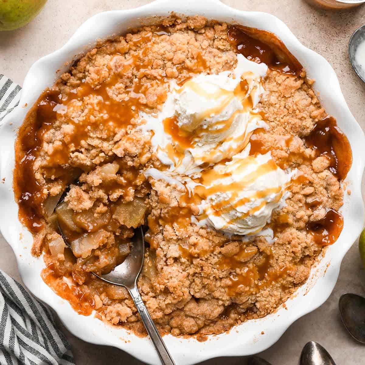 Pear Crumble in a pie dish with a spoon, two scoops of vanilla ice cream and caramel sauce