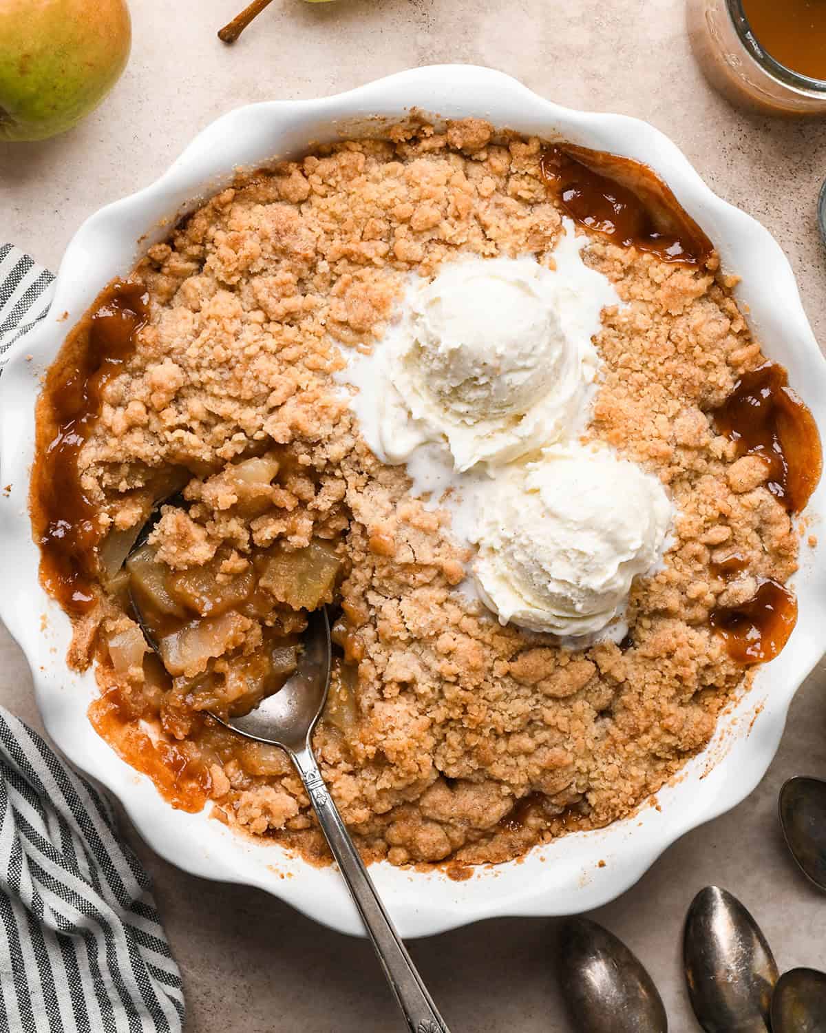 Pear Crumble in a pie dish with a spoon and two scoops of vanilla ice cream 