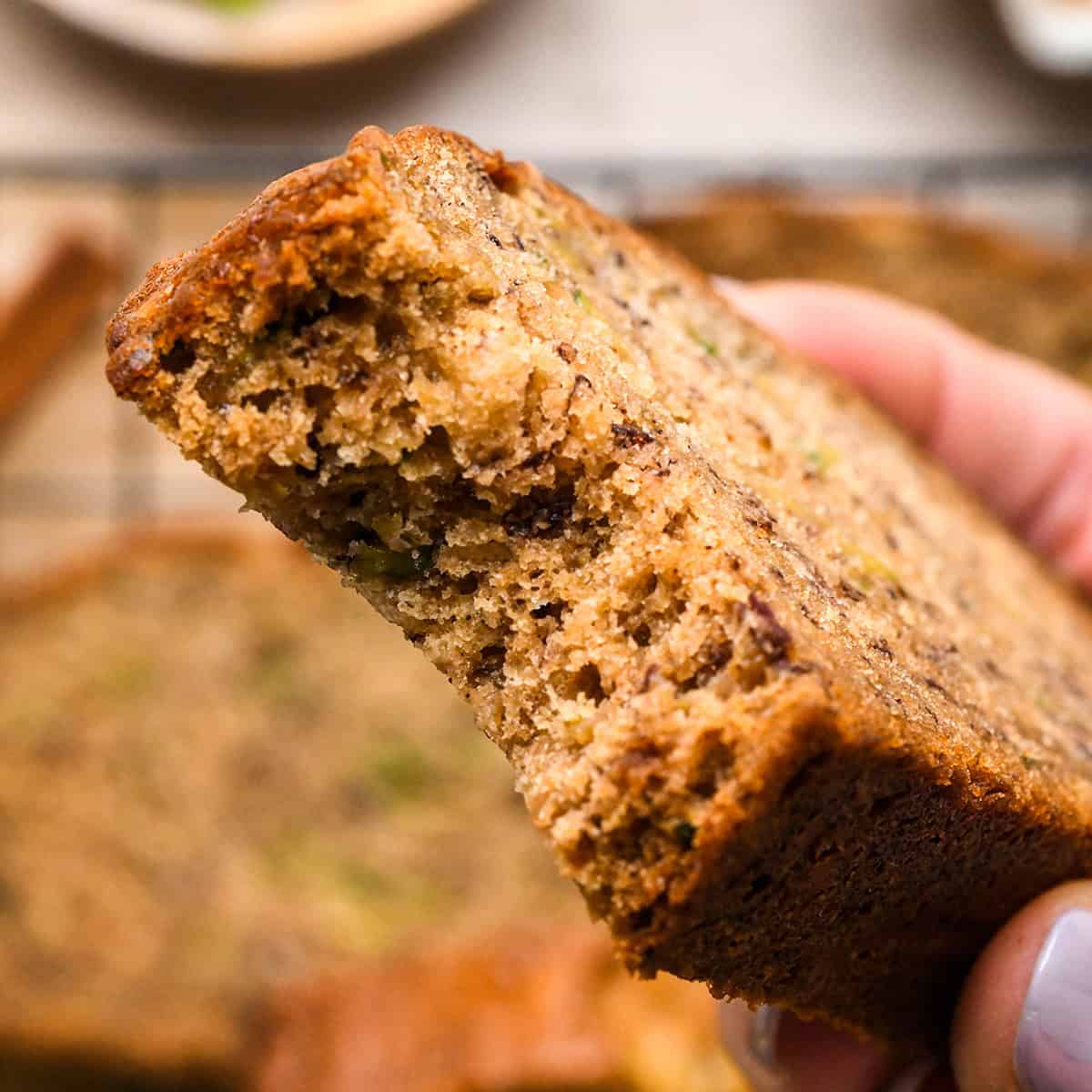 a hand holding a piece of Zucchini Banana Bread with a bite taken out of it