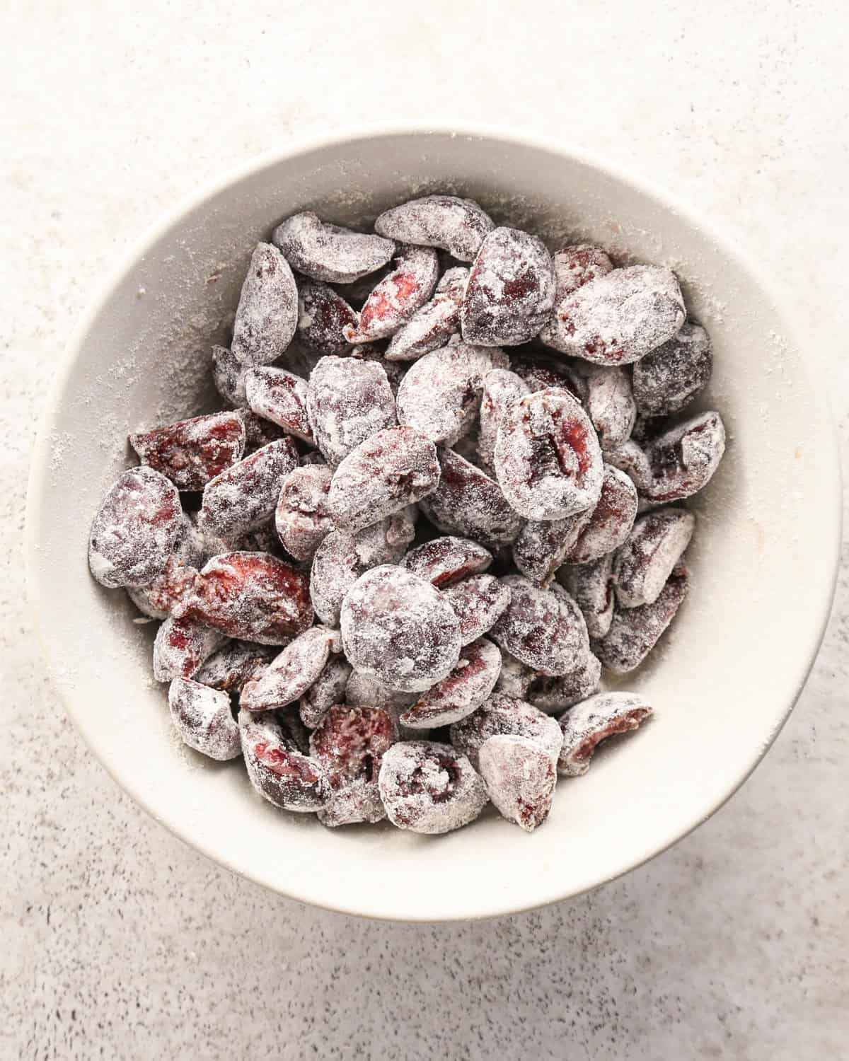 photo showing how to make cherry scones in a white bowl - halved cherries and flour in the bowl after mixing