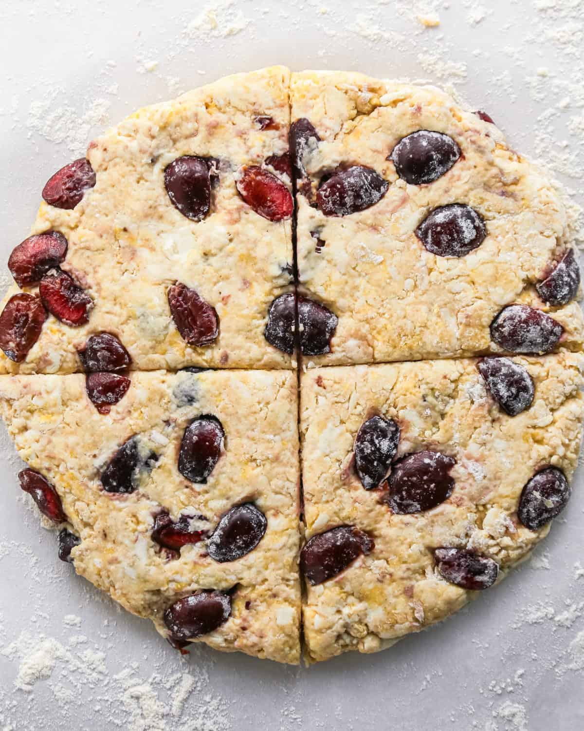 how to make cherry scones - scone dough with cherries formed into a round disc cut in quarters